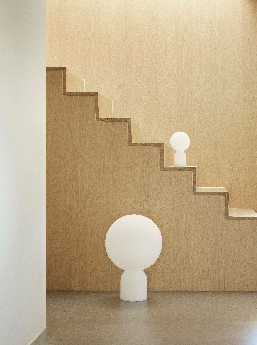 Zwei weiße Yo Lamp Tischleuchten von Normann Copenhagen vor einer Holztreppe und Wand.