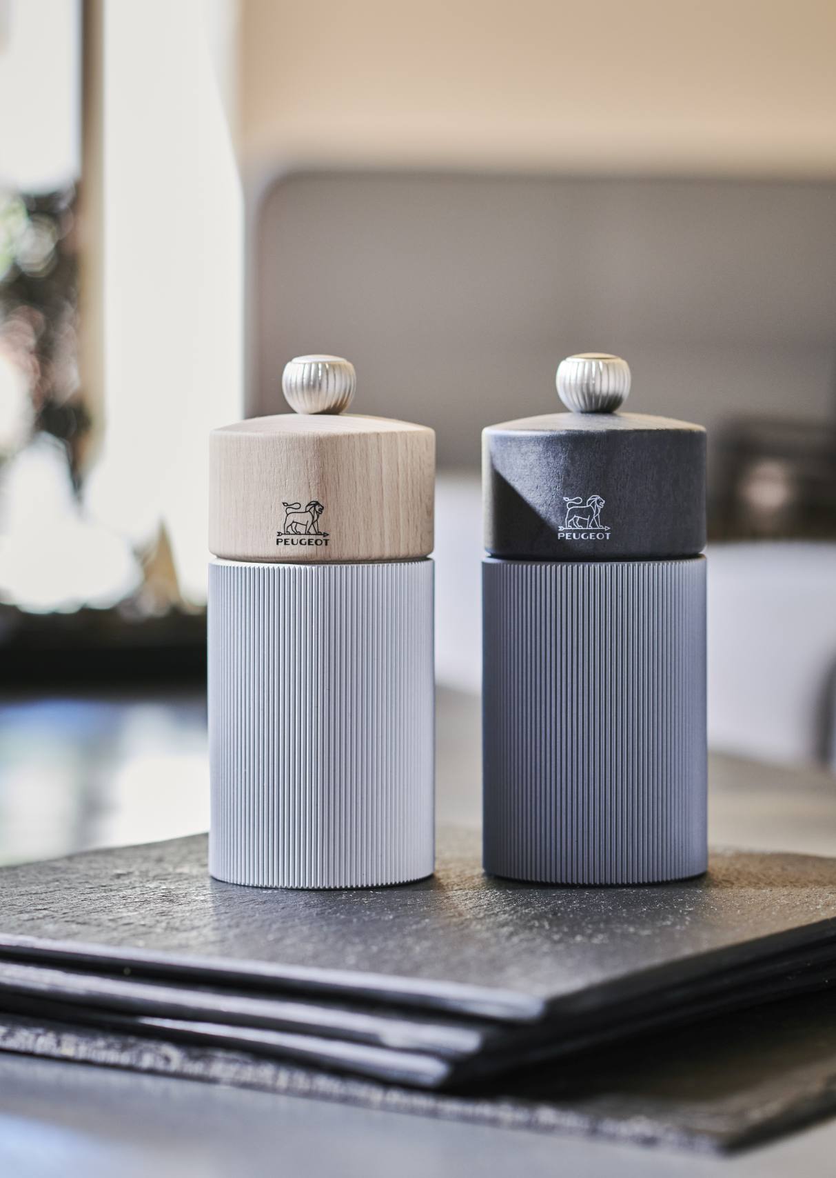 Zwei Line Salzmühlen H 12 cm von Peugeot, Aluminium und Naturholz, auf dunklem Untergrund.