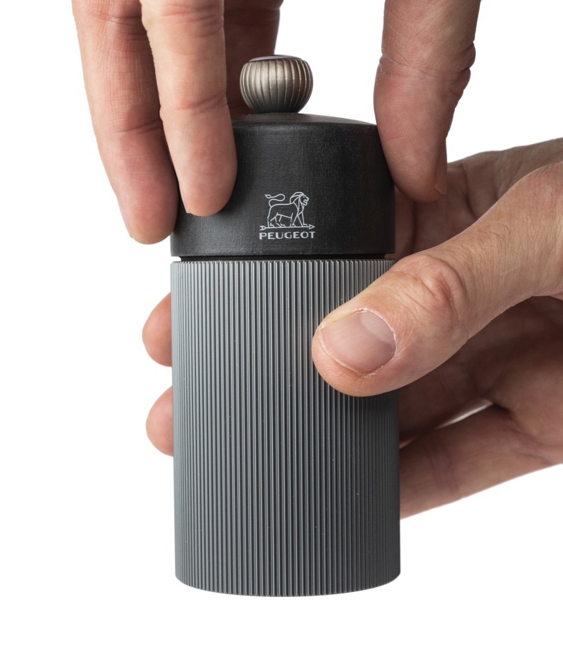 Hände bedienen Peugeot Line Pfeffermühle in Graphit und Carbon, hochwertige Küchenmühle für frischen Pfeffer.
