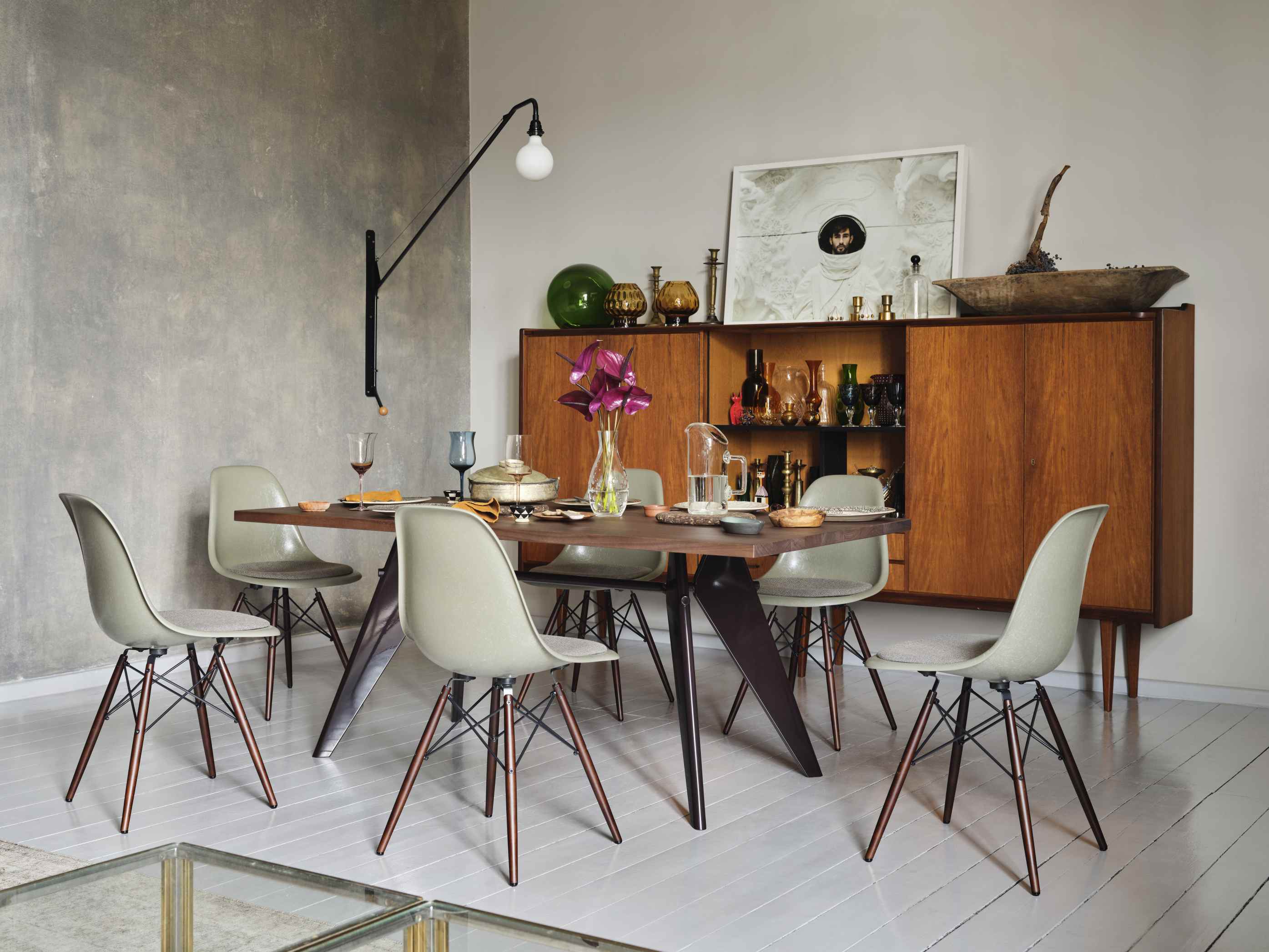 Esszimmer mit 6 Eames Plastic Side Chairs DSW in grau und EM Table in Nussbaum und schwarzem Gestell vor einem stilvoll arrangierten Highboard und Potence Wandleuchte.
