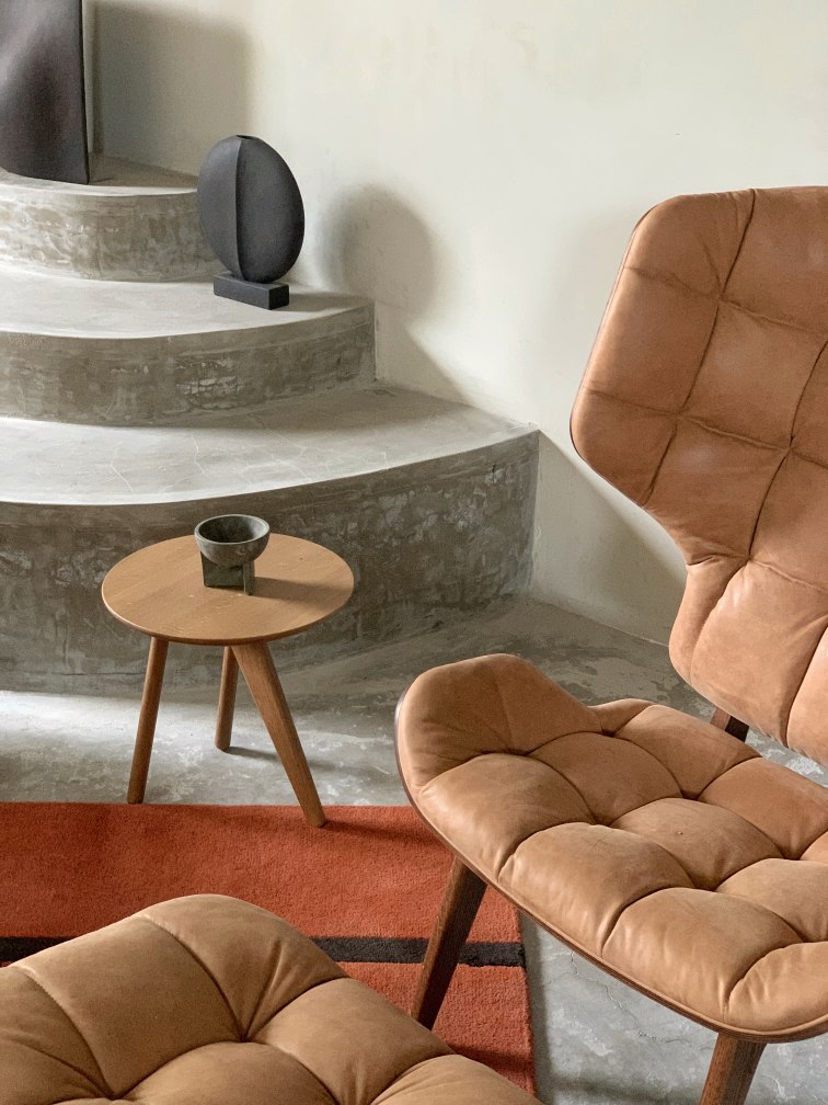 Nahaufnahme des NORR11 Mammoth Ottoman aus braunem Leder, kombiniert mit Beistelltisch und Sessel.