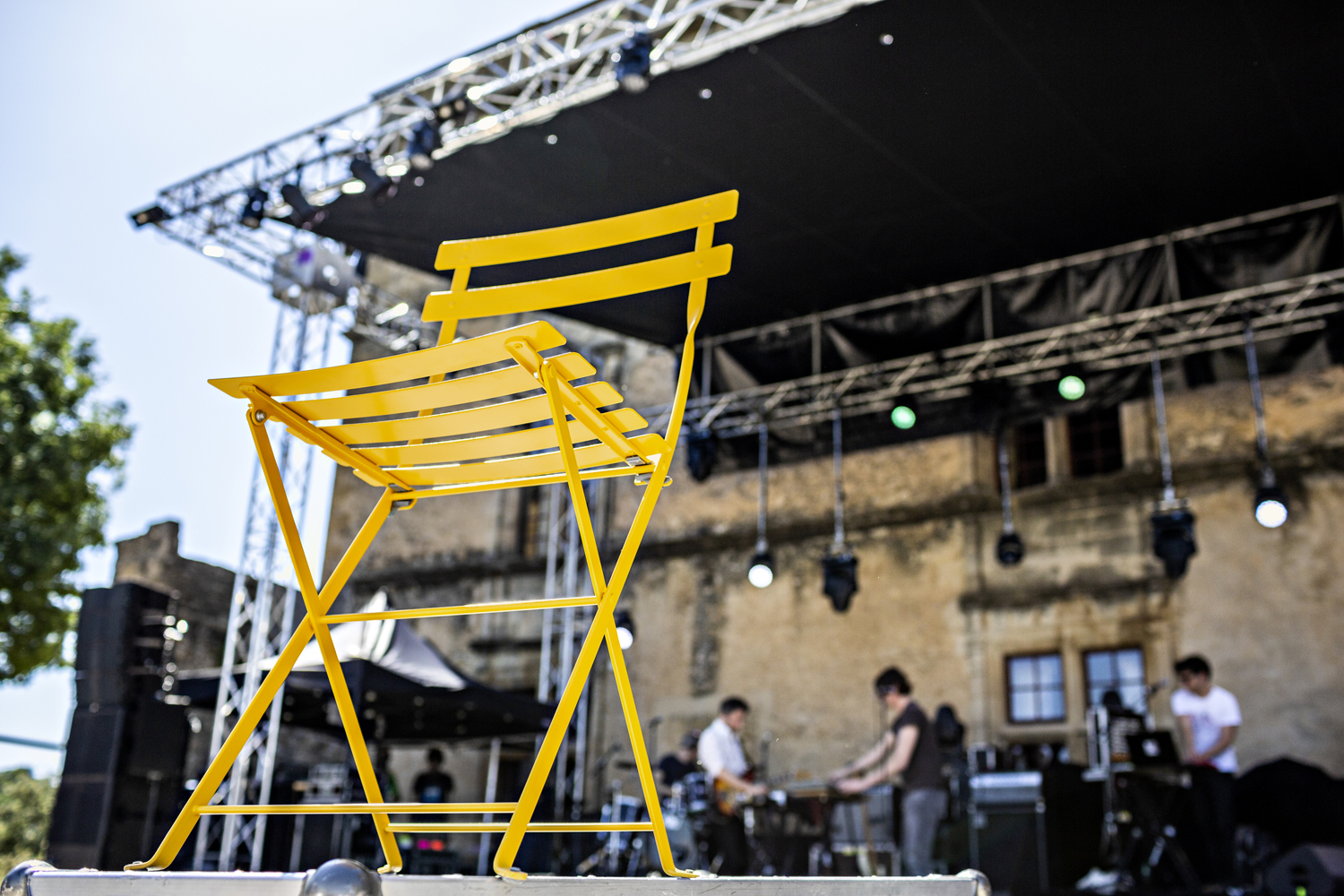 Gelber Bistro Gartenstuhl aus Metall von Fermob vor einer Bühne mit Musikern.