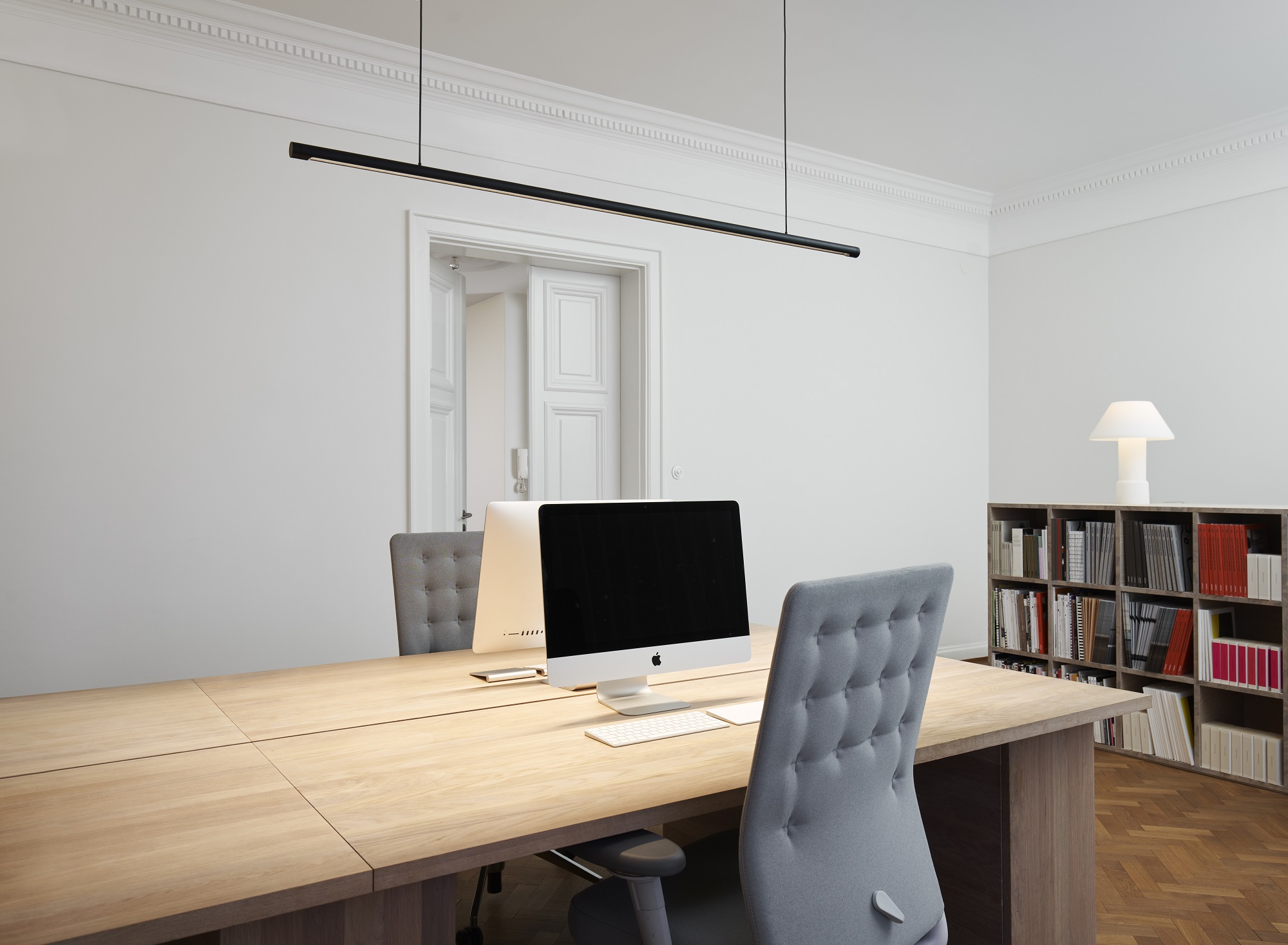 w181 Linier Pendelleuchte von wästberg über einem modernen Bürotisch mit Computern und Stühlen.