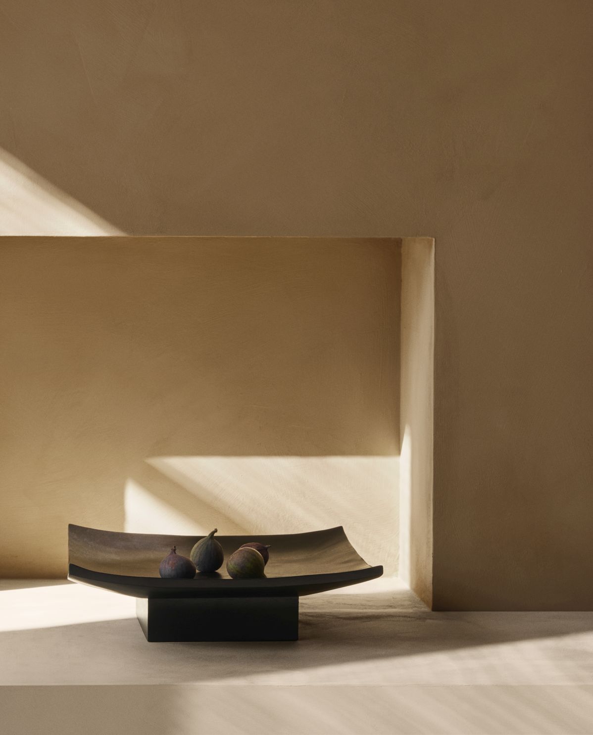 Audo Copenhagen Relevé Platte mit Feigen, moderne Dekoschale aus dunklem Holz auf Sockel.