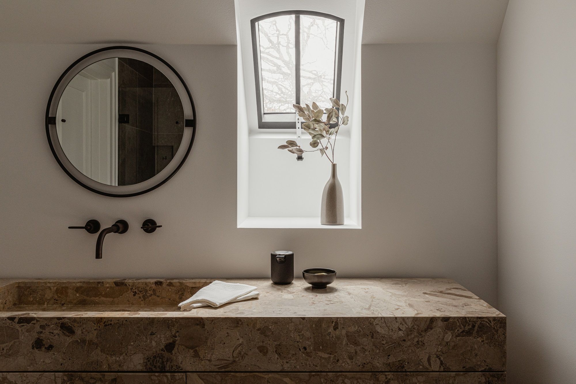 Badezimmer-Interieur mit rundem Nimbus Mirror Spiegel von Audo Copenhagen über einem Marmorwaschtisch mit Armatur.