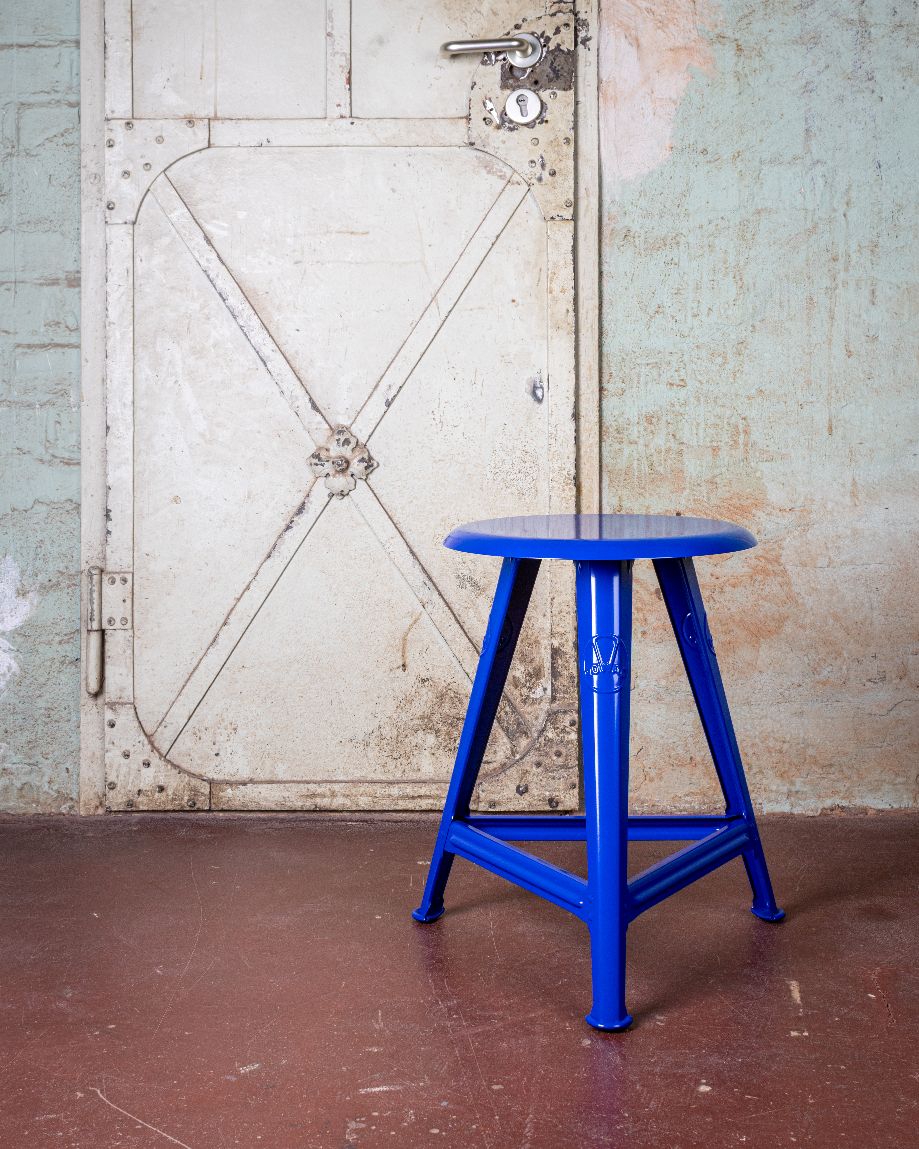 Blauer Rowac Schemel Modell IS, 48 cm hoch, vor einer alten Tür.