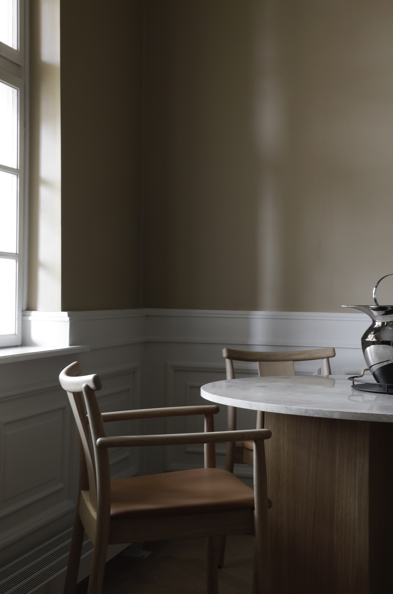 Merkur Dining Chair Stuhl mit Armlehnen von Audo Copenhagen am Esstisch, helle Holzstruktur und Ledersitz.
