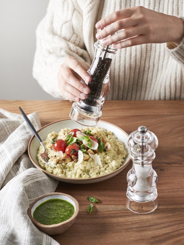 Nancy Pfeffermühle von Peugeot in Aktion: Eine Person würzt Risotto mit frischem Pfeffer.