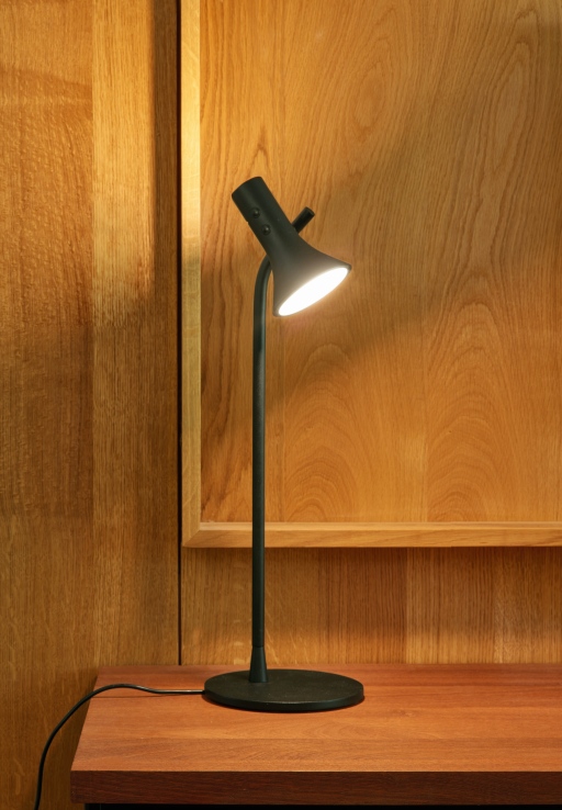 Schwarze Asha Tischleuchte von ligne roset auf einem Holztisch vor einer Holzvertäfelung.