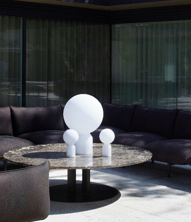 Normann Copenhagen Yo Lamp Large Akkuleuchte auf Marmortisch mit Sofa im Hintergrund, moderne Tischleuchte für Wohnzimmer.