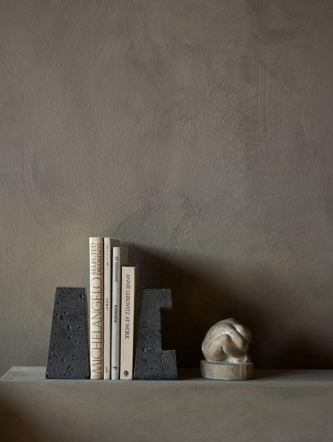 Converge Buchstützen von Audo Copenhagen aus dunklem Lavastein mit Büchern und Skulptur auf einem Regal.