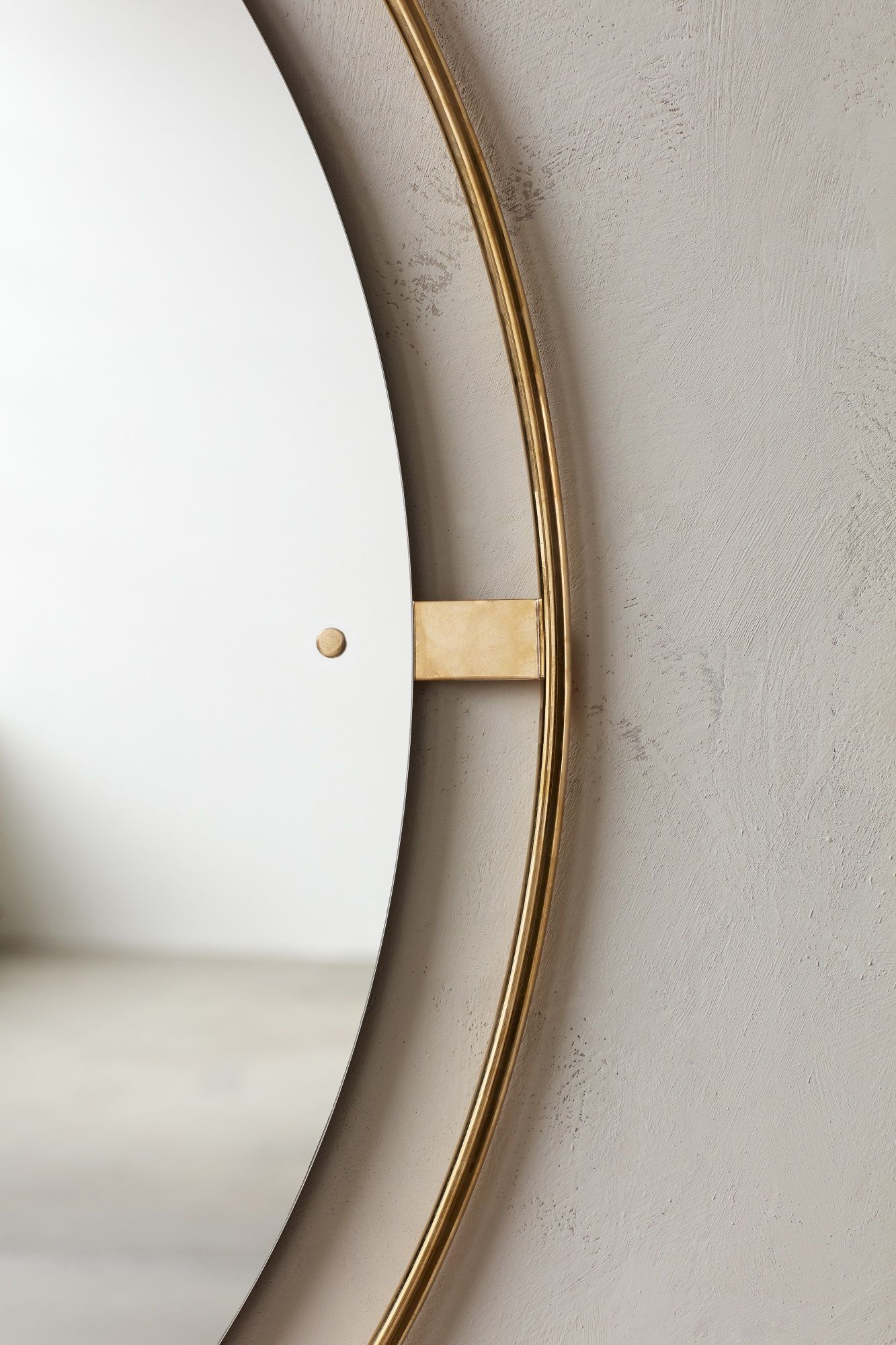 Detailaufnahme des Audo Copenhagen Nimbus Mirror Spiegels mit goldenem Rahmen an einer hellgrauen Wand.