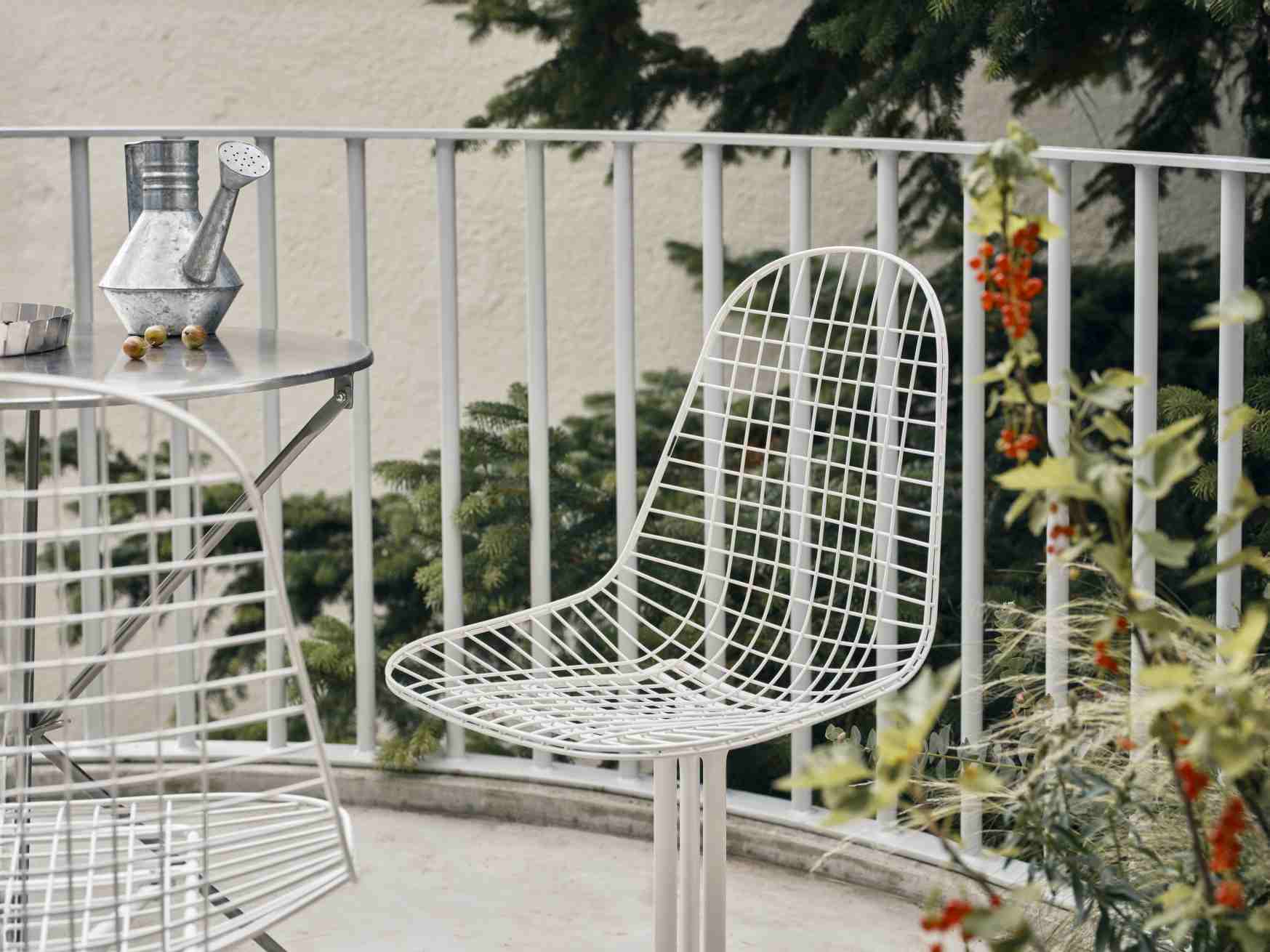 Nahaufnahme eines weißen DKL Wire Chair Stuhls von Vitra auf einem Balkon mit Tisch und Pflanzen.
