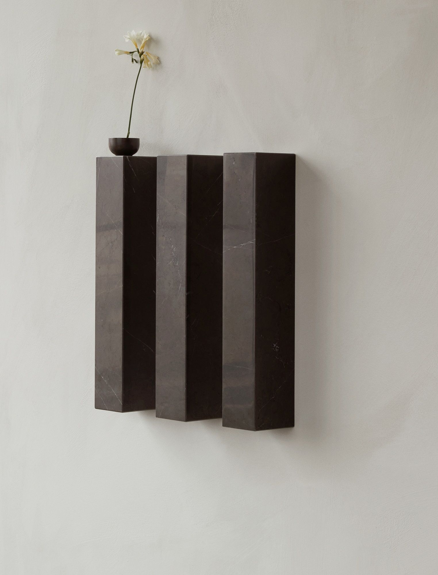 Audo Copenhagen Plinth Shelf Regal aus Marmor mit Blume an der Wand.