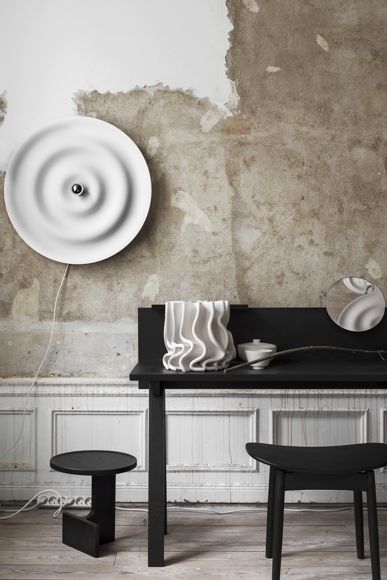Weiße w171 Alma Wandleuchte von wästberg an einer Wand mit minimalistischer Tischdekoration und schwarzen Hockern.
