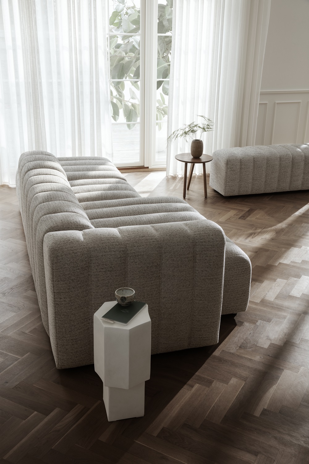 Norr11 Fin Beistelltisch aus Travertin neben modularem Sofa in hellem Wohnzimmer mit Parkettboden.