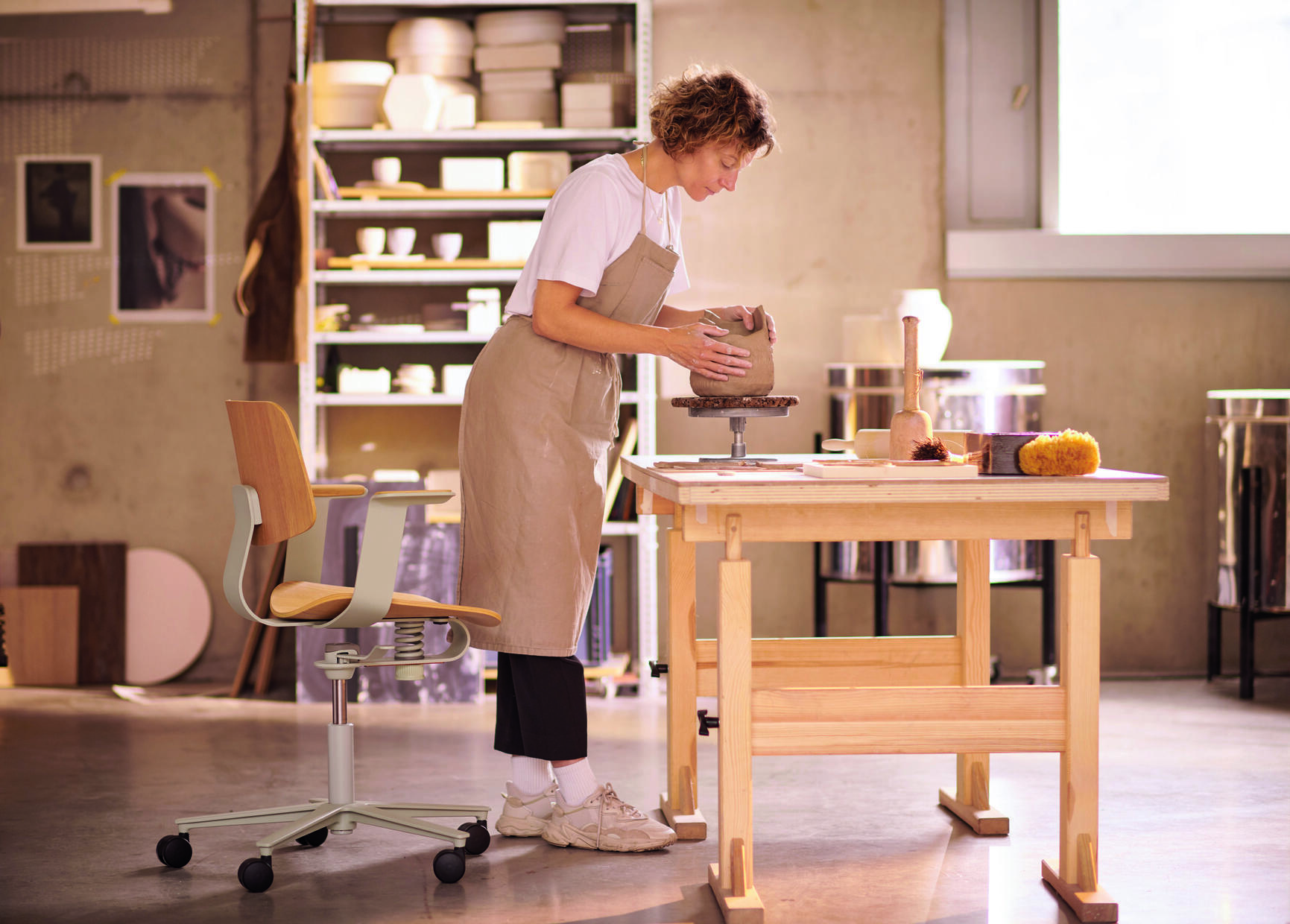 Wilkhahn WiChair Drehstuhl im Atelier: Frau arbeitet am Tisch, im Hintergrund der Bürostuhl.