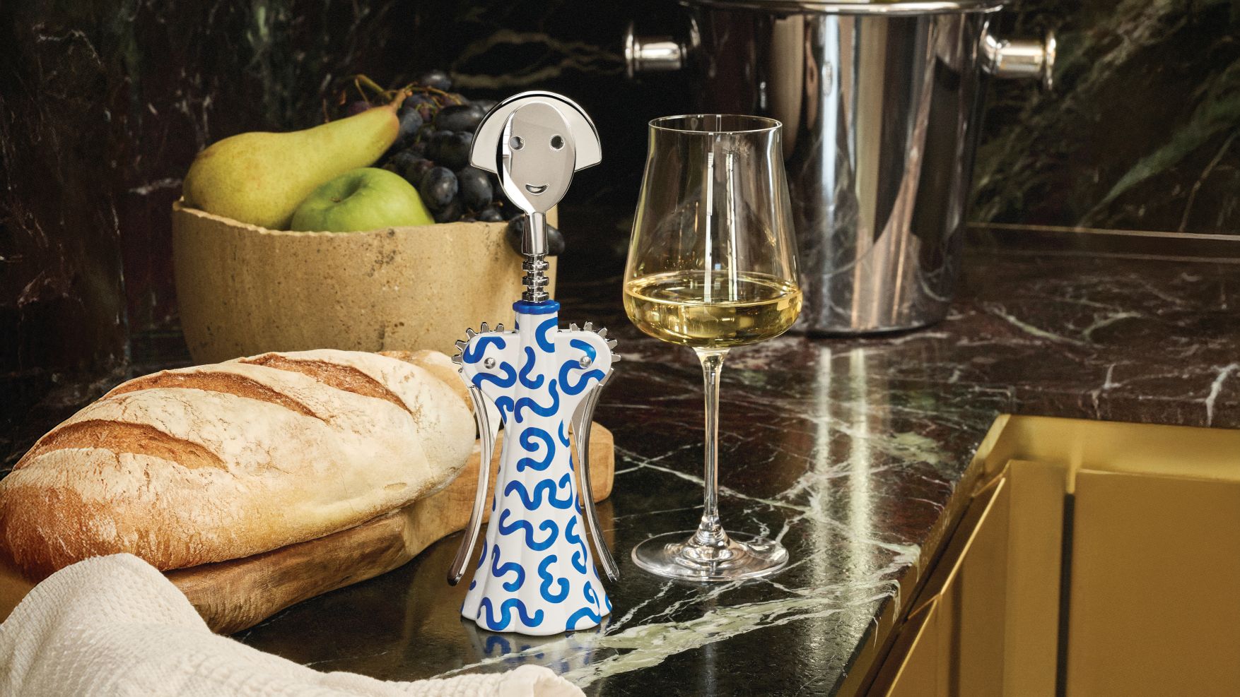 Alessi Anna G. Korkenzieher Delft mit Brot, Obst und Weißweinglas auf einer Marmoroberfläche.