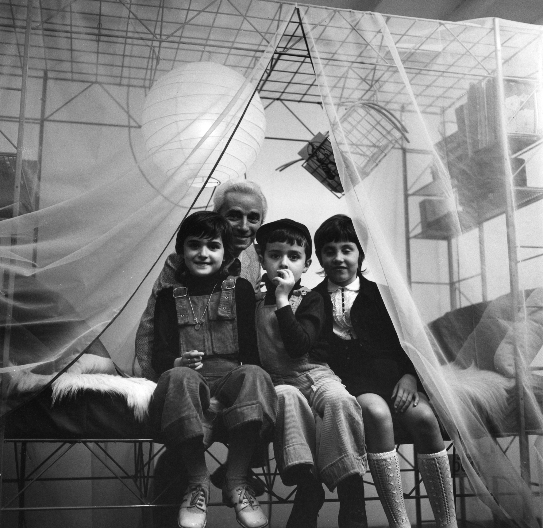 Schwarz-Weiß-Foto: Abitacolo Multifunktionsbett von Rexite mit drei Kindern und einem Erwachsenen unter einem Baldachin.