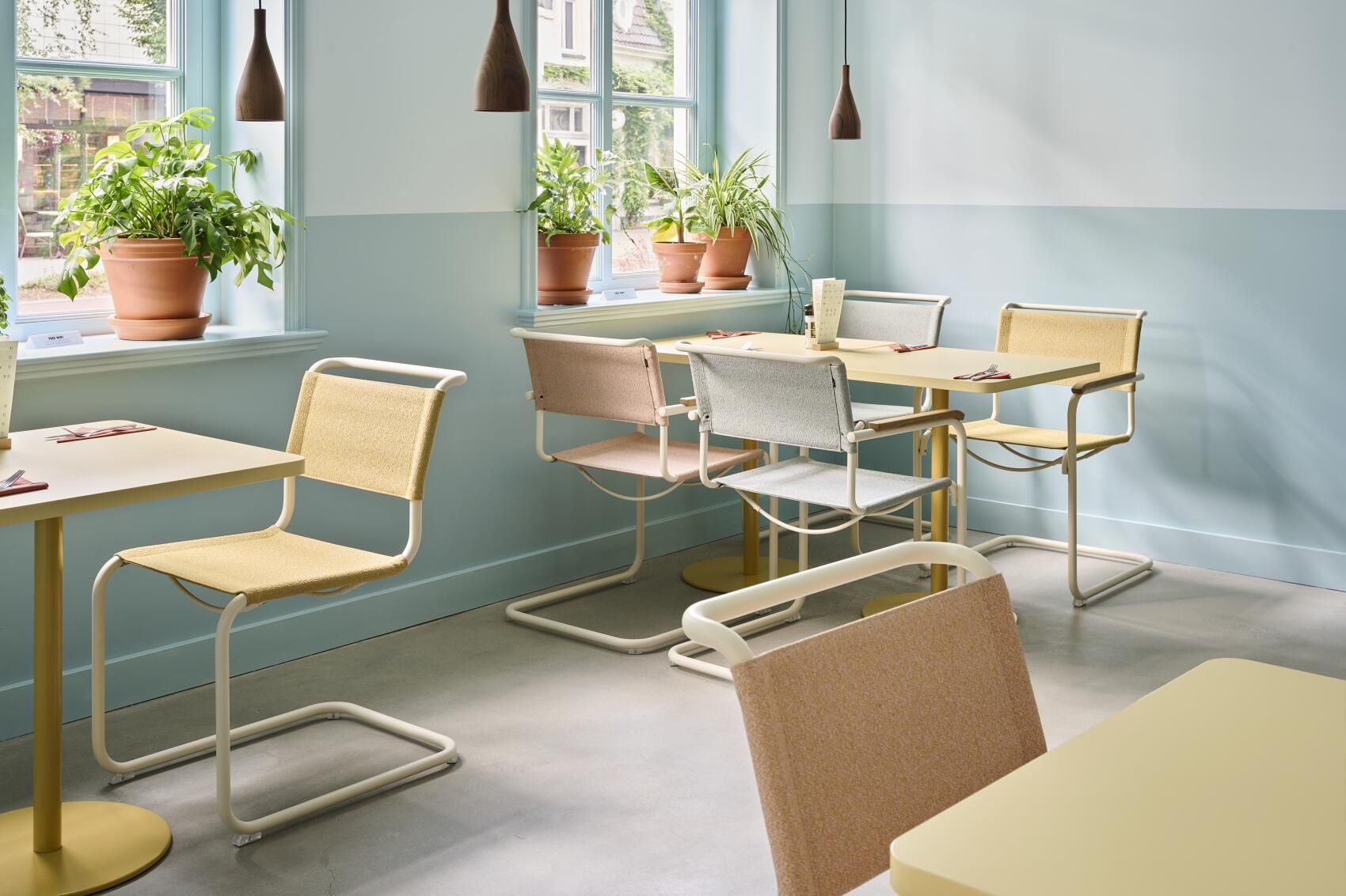 Innenaufnahme eines Restaurants mit mehreren Thonet S 33 Freischwinger Stühlen in verschiedenen Farben an gelben Tischen.