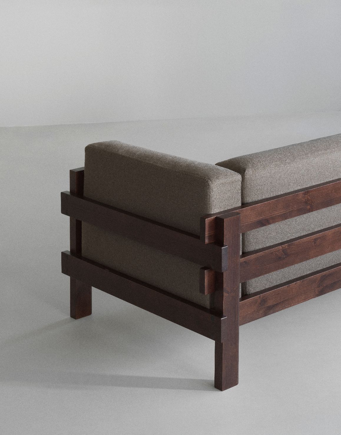 Detailaufnahme des Kube Sofas von Normann Copenhagen mit braunem Holzrahmen und grauen Polstern.