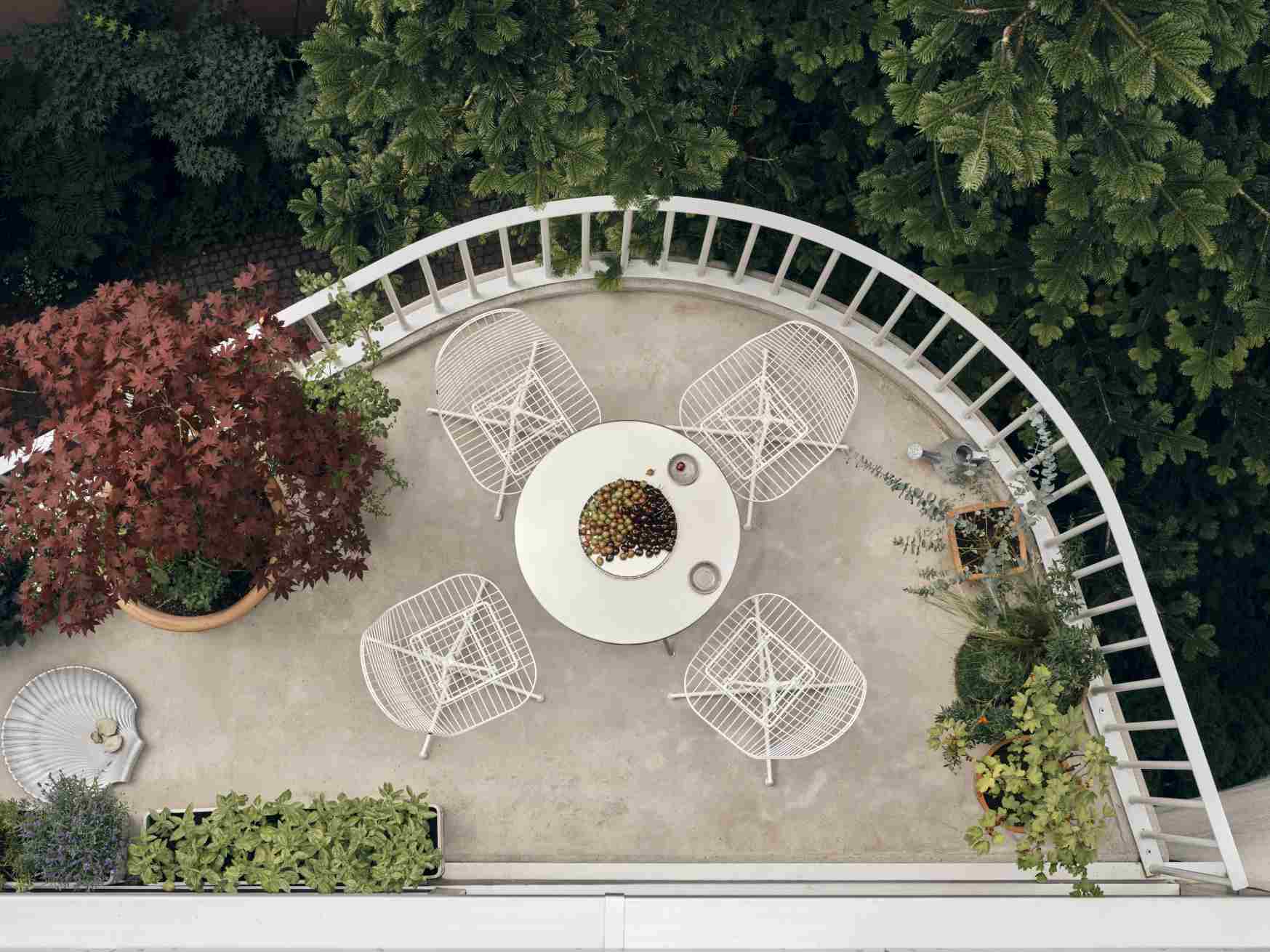 Draufsicht: Vier weiße Vitra DKL Wire Chairs um einen runden Tisch auf einer Dachterrasse.