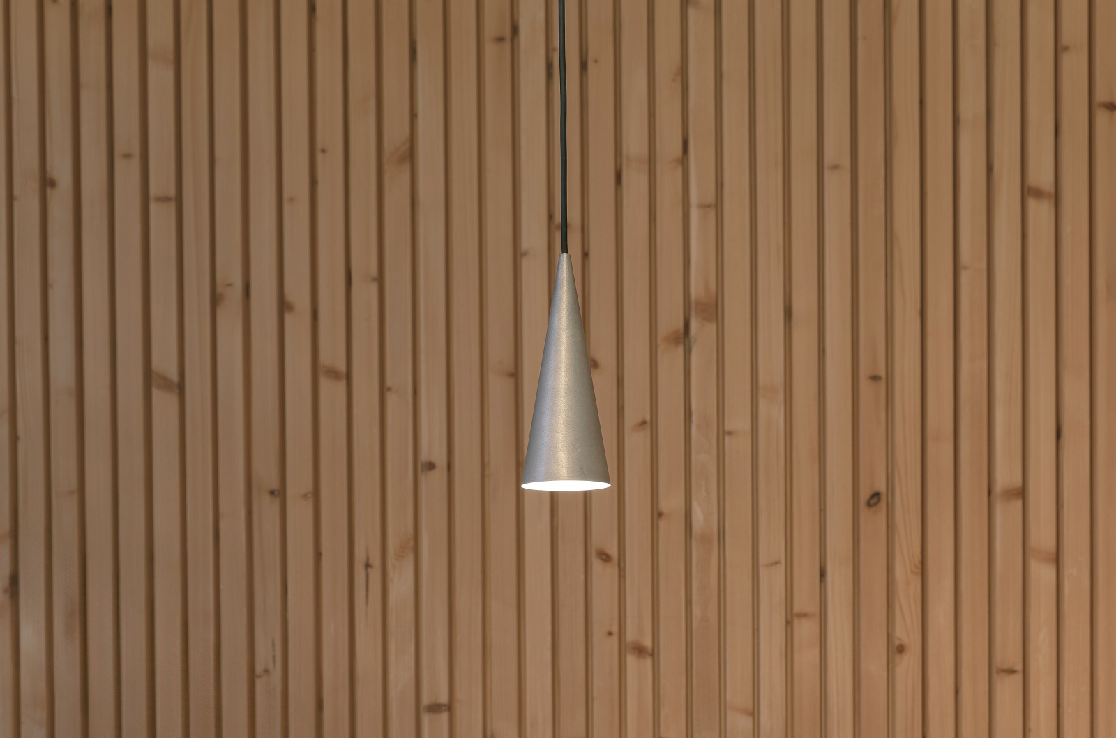 w201 S1 Pendelleuchte von wästberg, Kegelförmige Hängelampe aus Aluminium vor einer Holzwand.