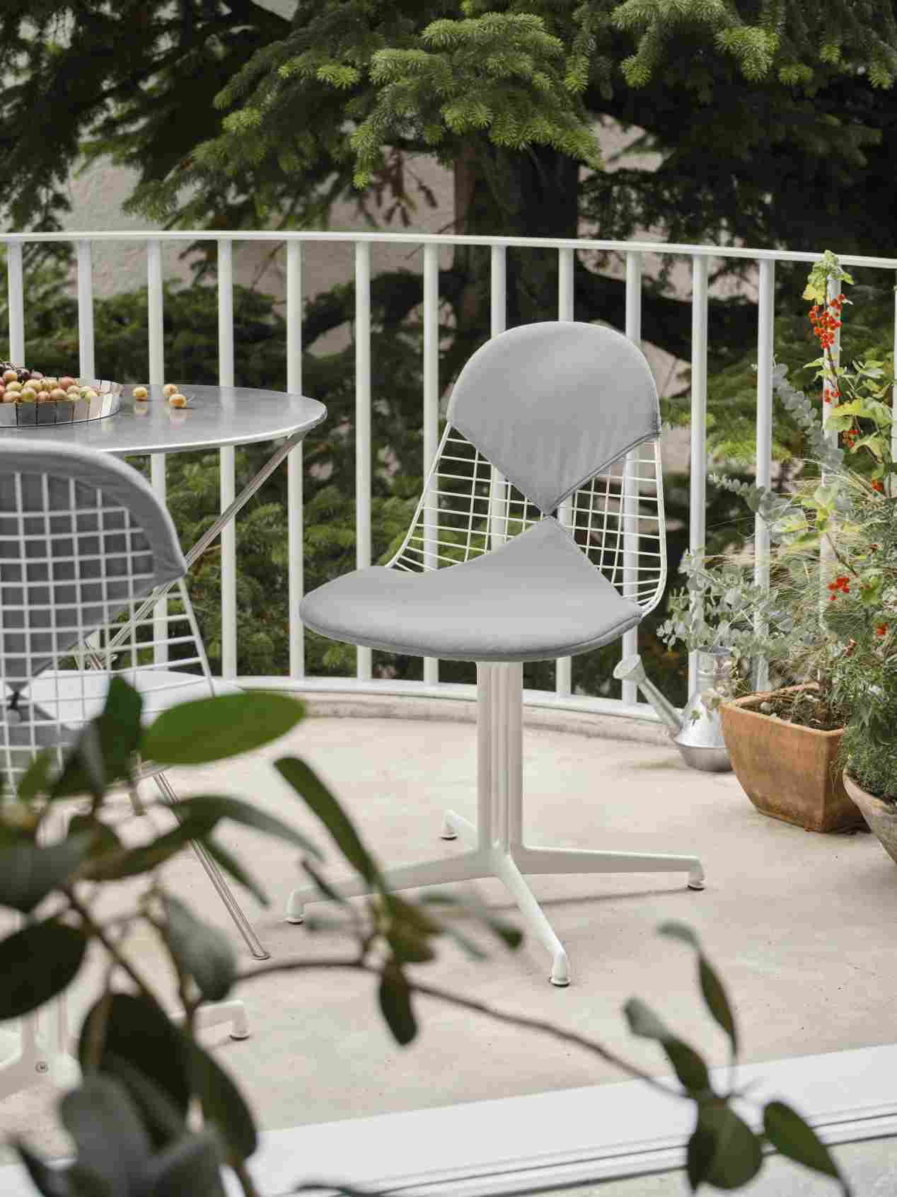Vitra Wire Chair Bikini Outdoor mit grauem Sitzkissen auf einem Balkon mit Tisch und Pflanzen.