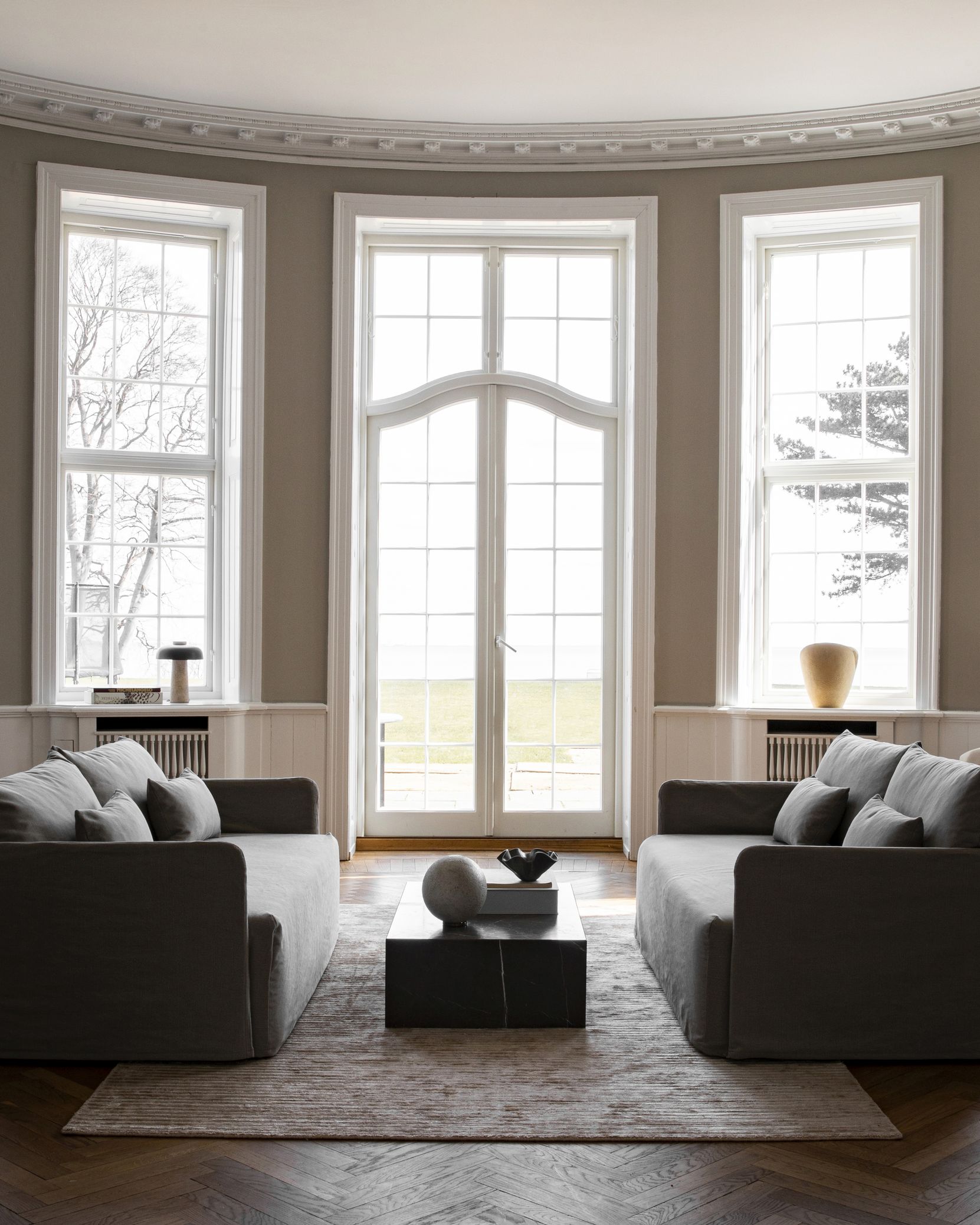 Helles Wohnzimmer mit zwei grauen Offset Sofas von Audo Copenhagen und einem dunklen Couchtisch.
