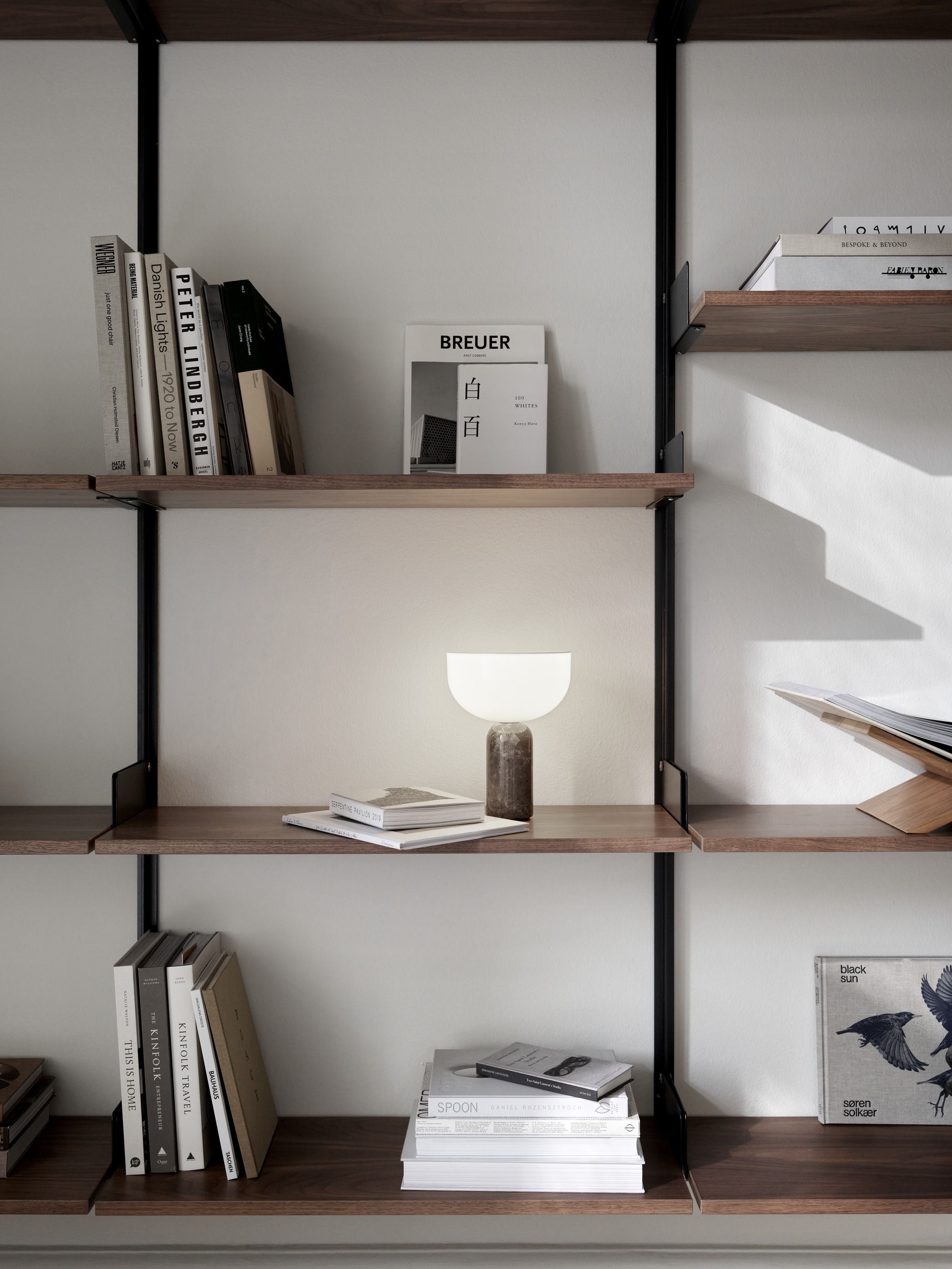New Works Kizu Tischleuchte auf Regal mit Büchern, modernes Design, stimmungsvolle Beleuchtung.