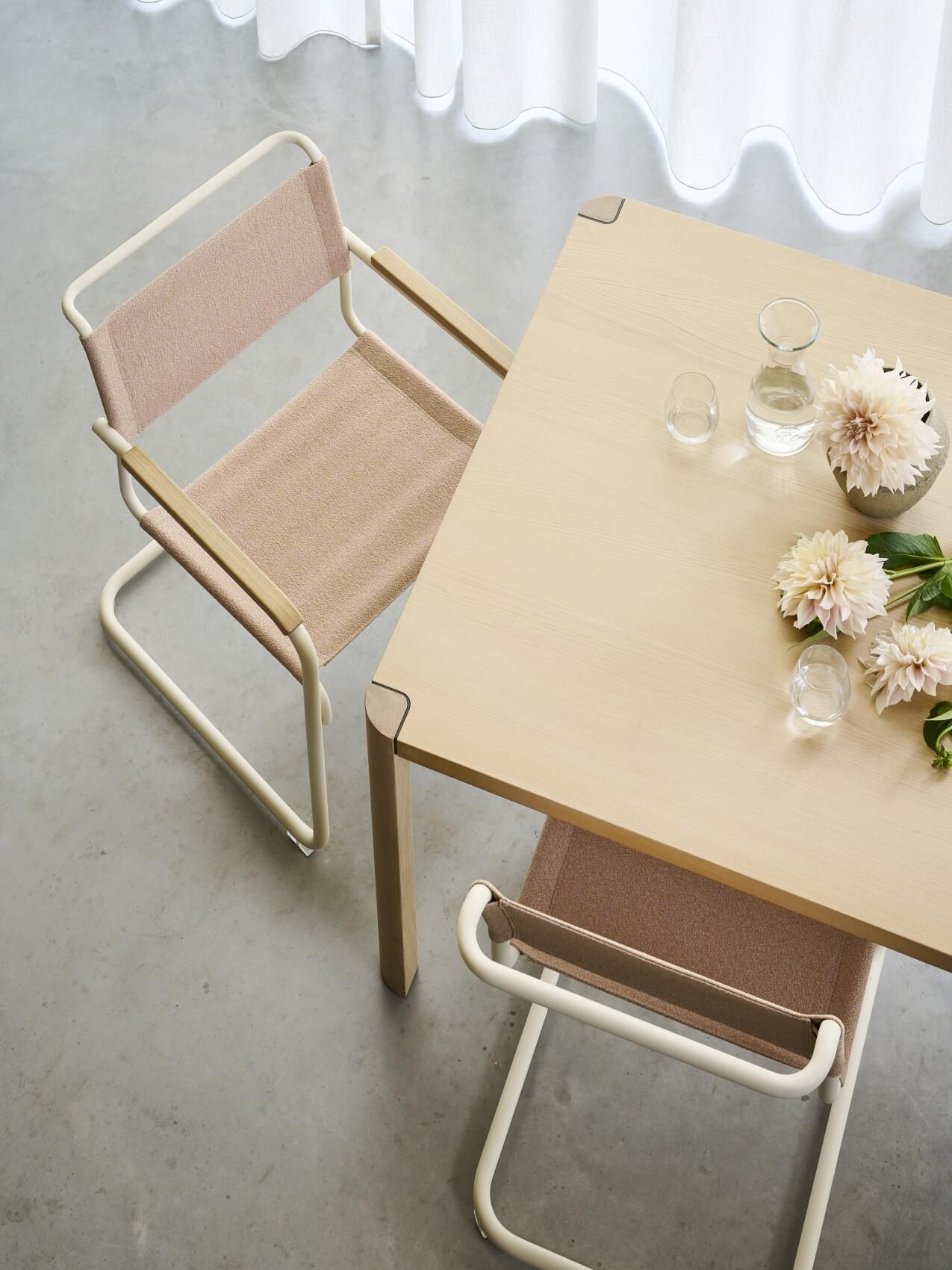 Thonet S 34 Freischwinger Stuhl mit Armlehnen und beigem Stoffbezug an Esstisch mit Blumendekoration.