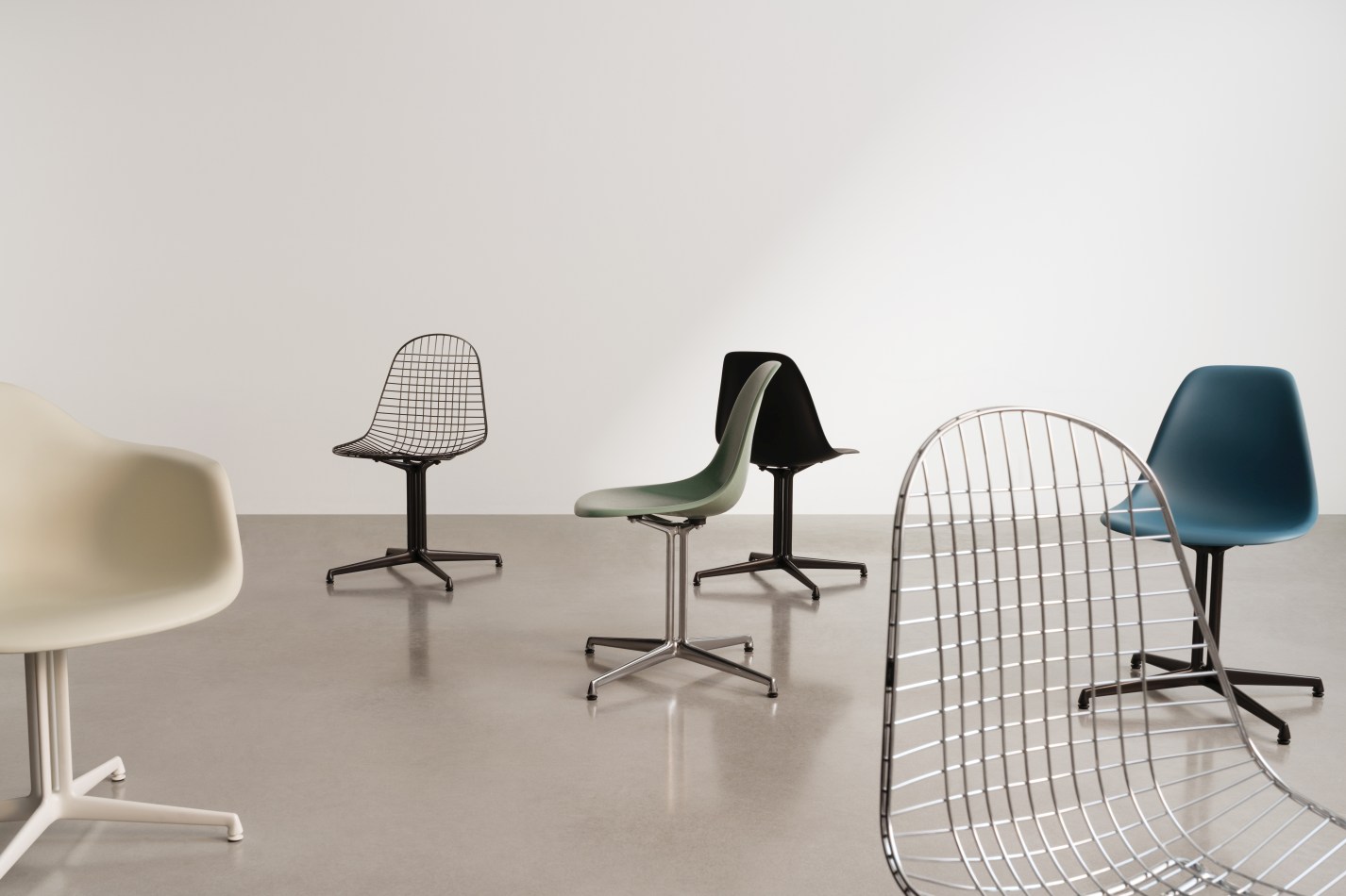 Mehrere Vitra Stühle, darunter der DKL Wire Chair, in verschiedenen Farben und Ausführungen auf grauem Boden.