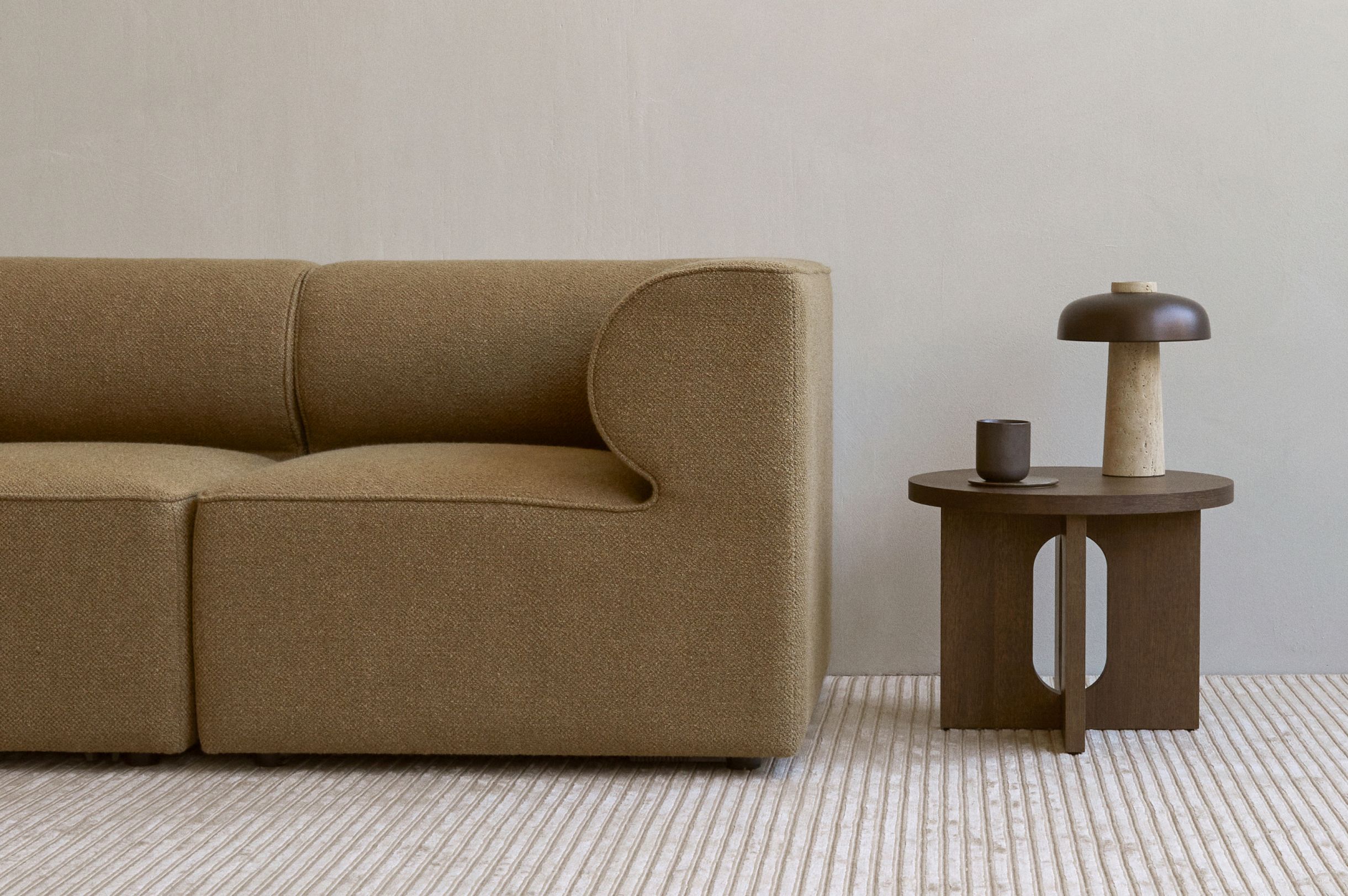 Androgyne Beistelltisch von Audo, brauner Holztisch mit Lampe und Tasse neben beigem Sofa.