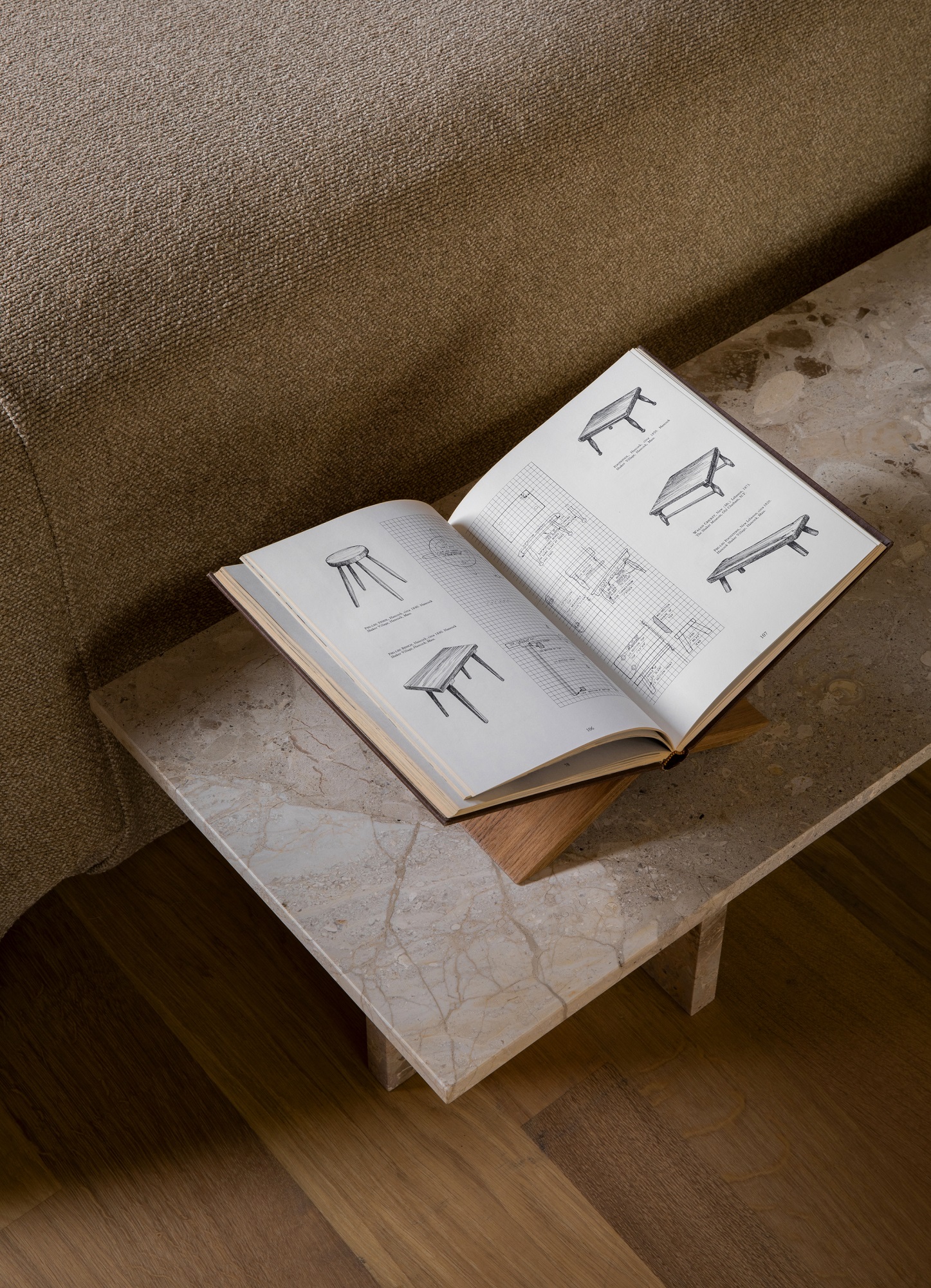 Androgyne Couchtisch von Audo Copenhagen aus Marmor mit Buch über Tischdesign neben Sofa.
