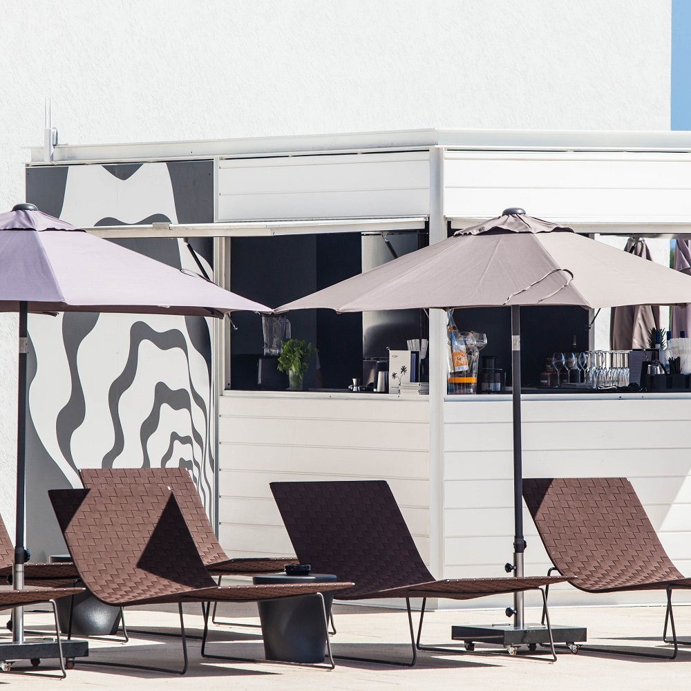 Andreu World Trenza Outdoor Liegen mit Sonnenschirmen vor einem modernen Gebäude für entspannte Stunden im Freien.