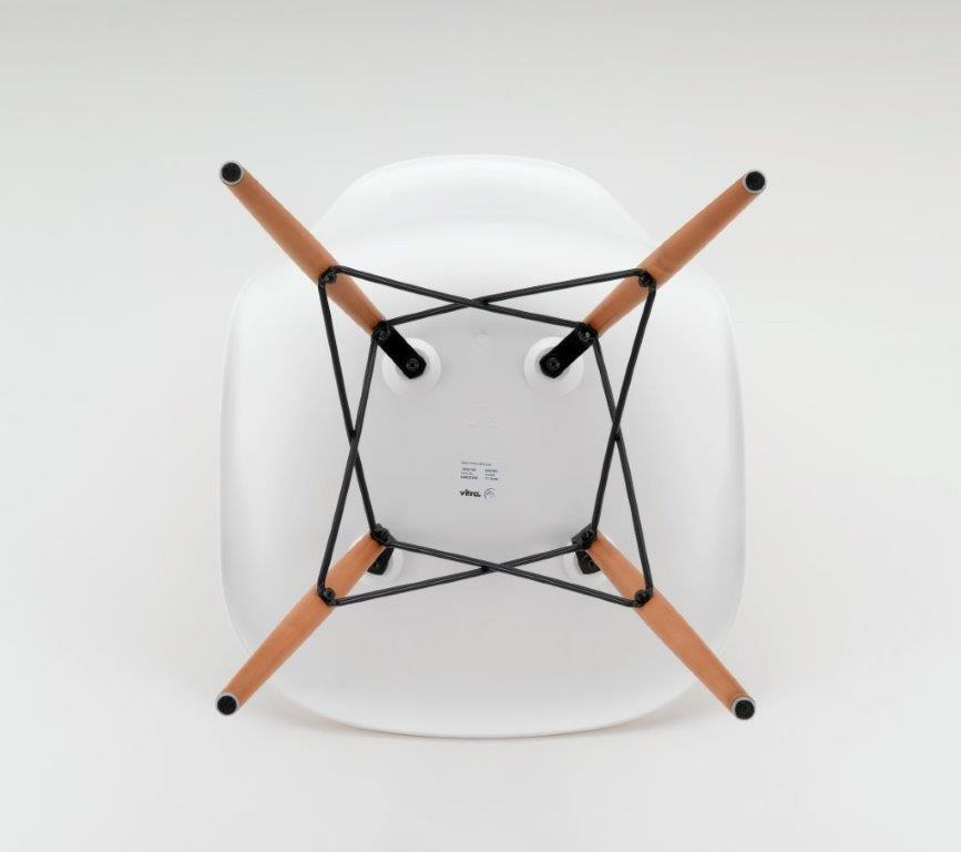 Detailaufnahme der Unterseite eines weißen Eames Plastic Side Chair DSW Stuhls von Vitra mit Holzbeinen.