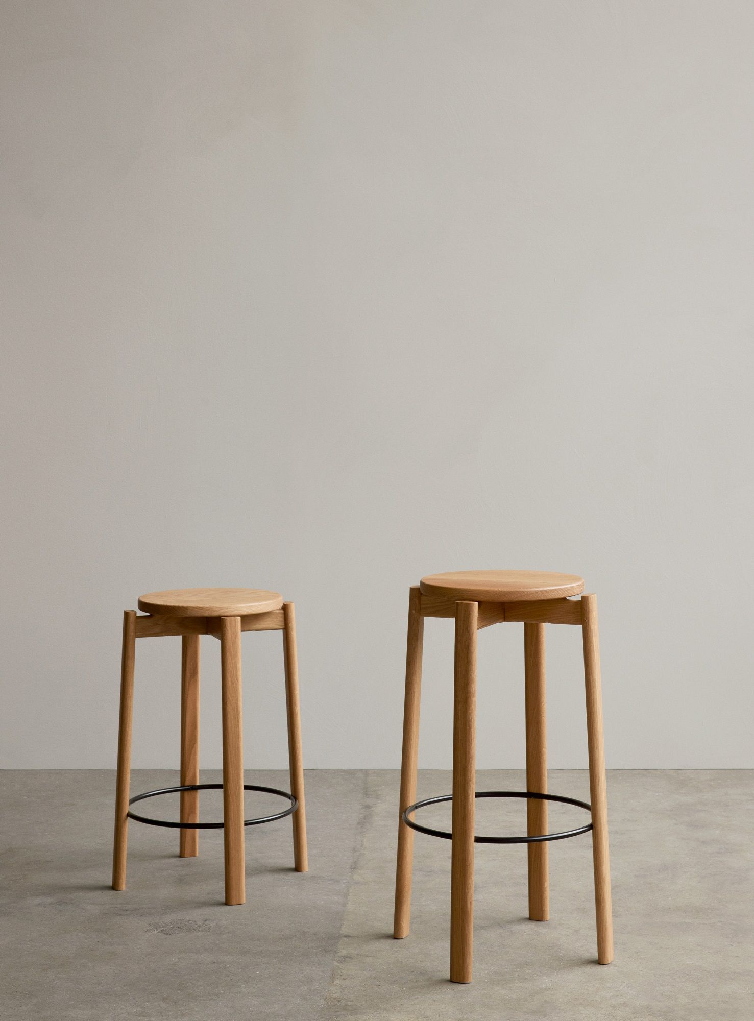 Zwei Audo Copenhagen Barhocker "Passage Bar Stool" aus hellem Holz mit schwarzer Fußstütze.