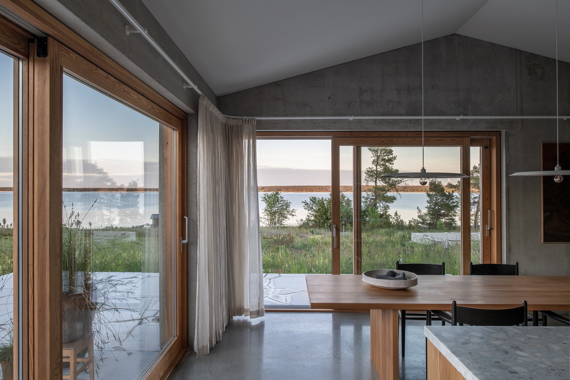 Helle Esszimmer-Szene mit w171 Alma Pendelleuchte von wästberg über einem Holztisch mit Seeblick.