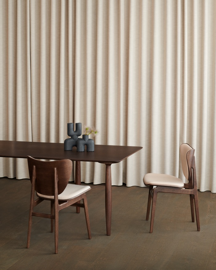 NORR11 Elephant Dining Chair, vollgepolstert, aus Holz mit beigem Sitzpolster an dunklem Esstisch.