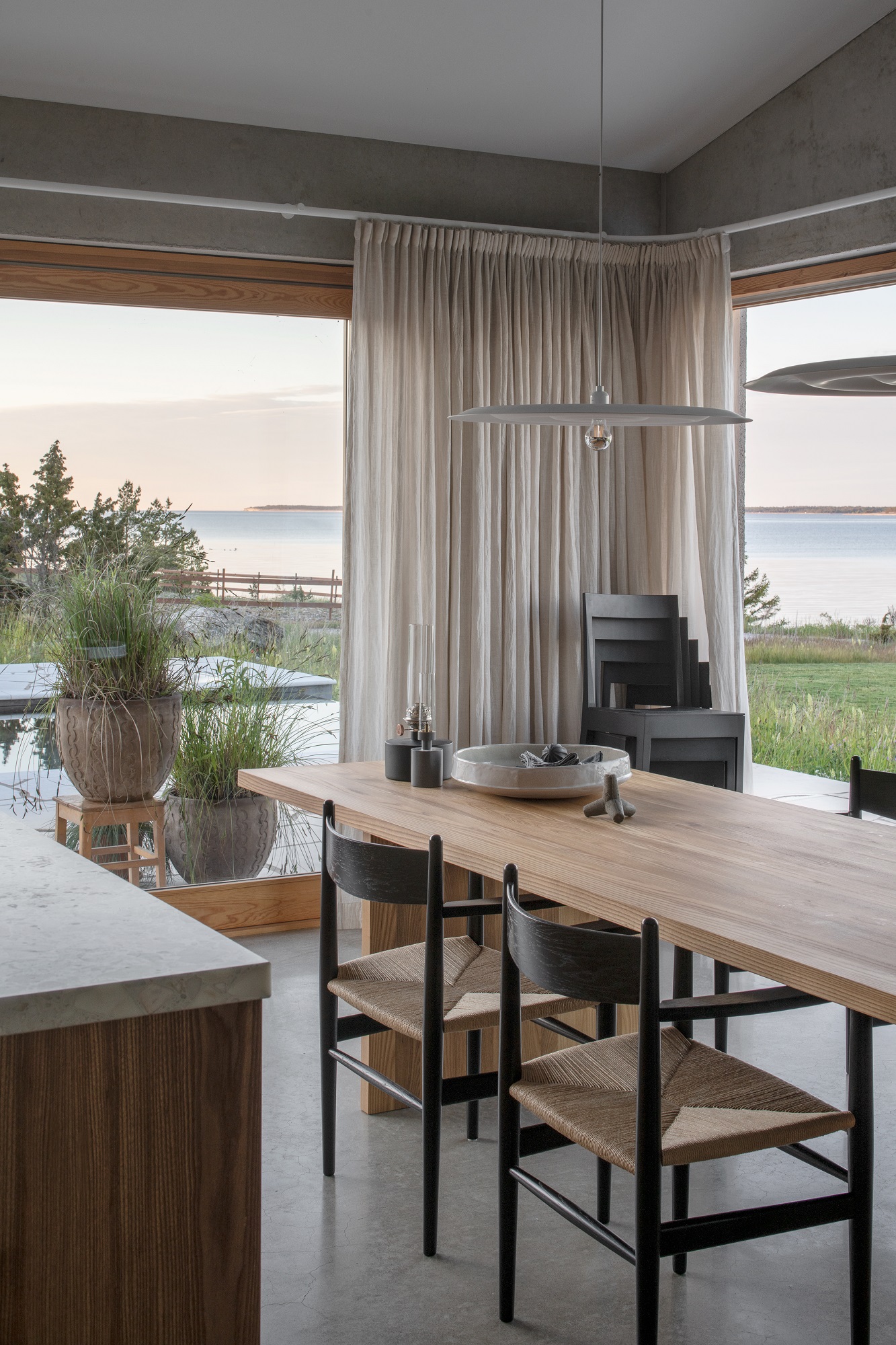 Helle wästberg w171 Alma Pendelleuchte über Esstisch mit Stühlen in modernem Esszimmer mit Meerblick.