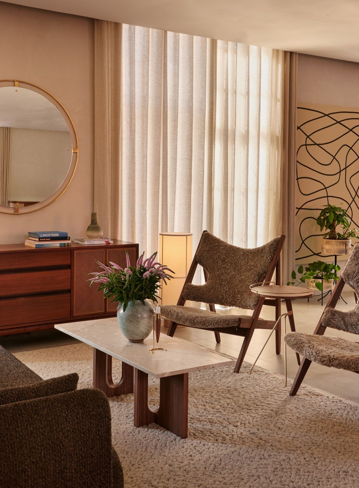 Wohnzimmer Interieur mit Audo Copenhagen Nimbus Spiegel, Holzkommode, Marmortisch und bequemen Sesseln.