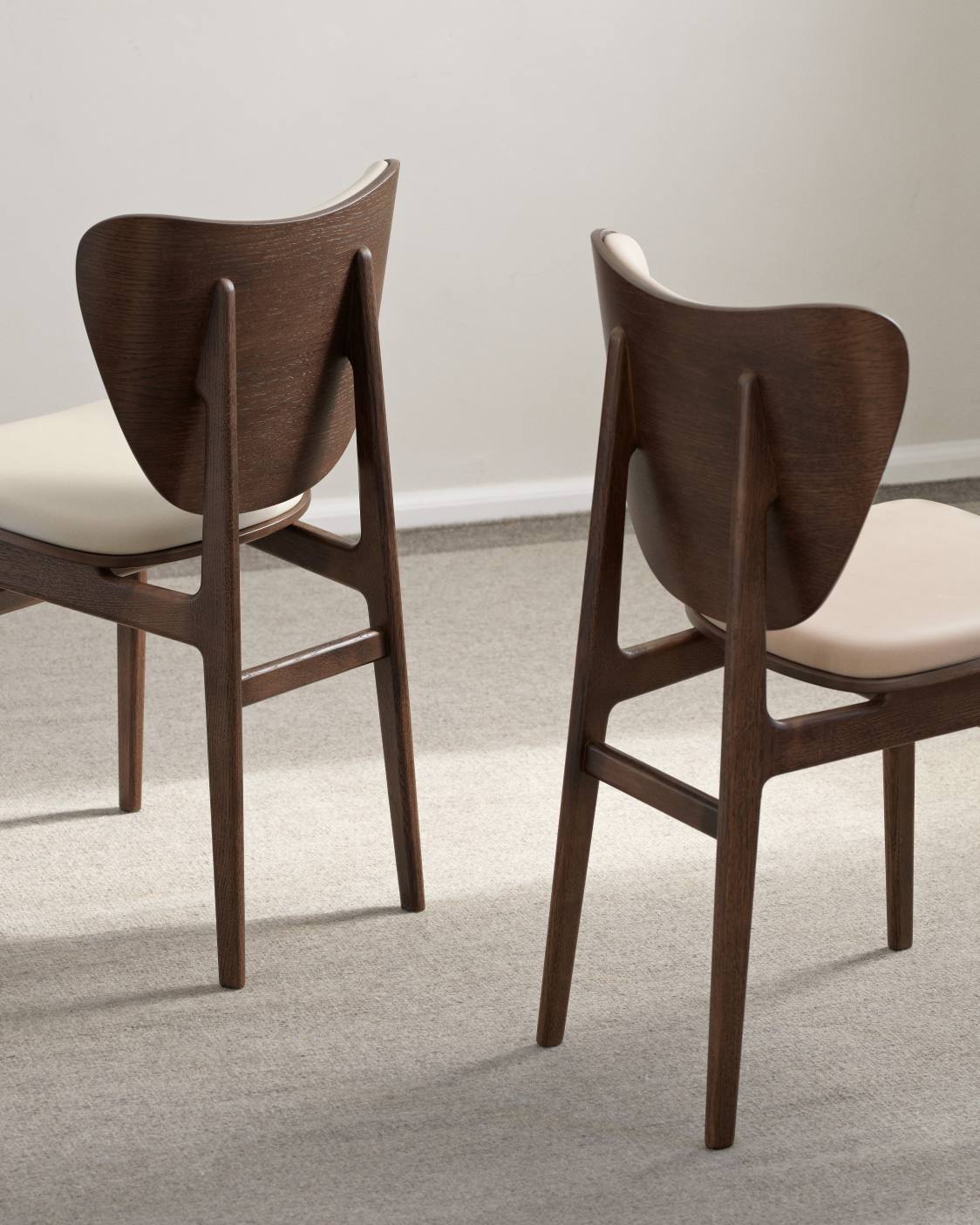 Zwei NORR11 Elephant Dining Chairs mit Frontpolsterung, braunem Holzrahmen und beigen Sitzen, Rückansicht.
