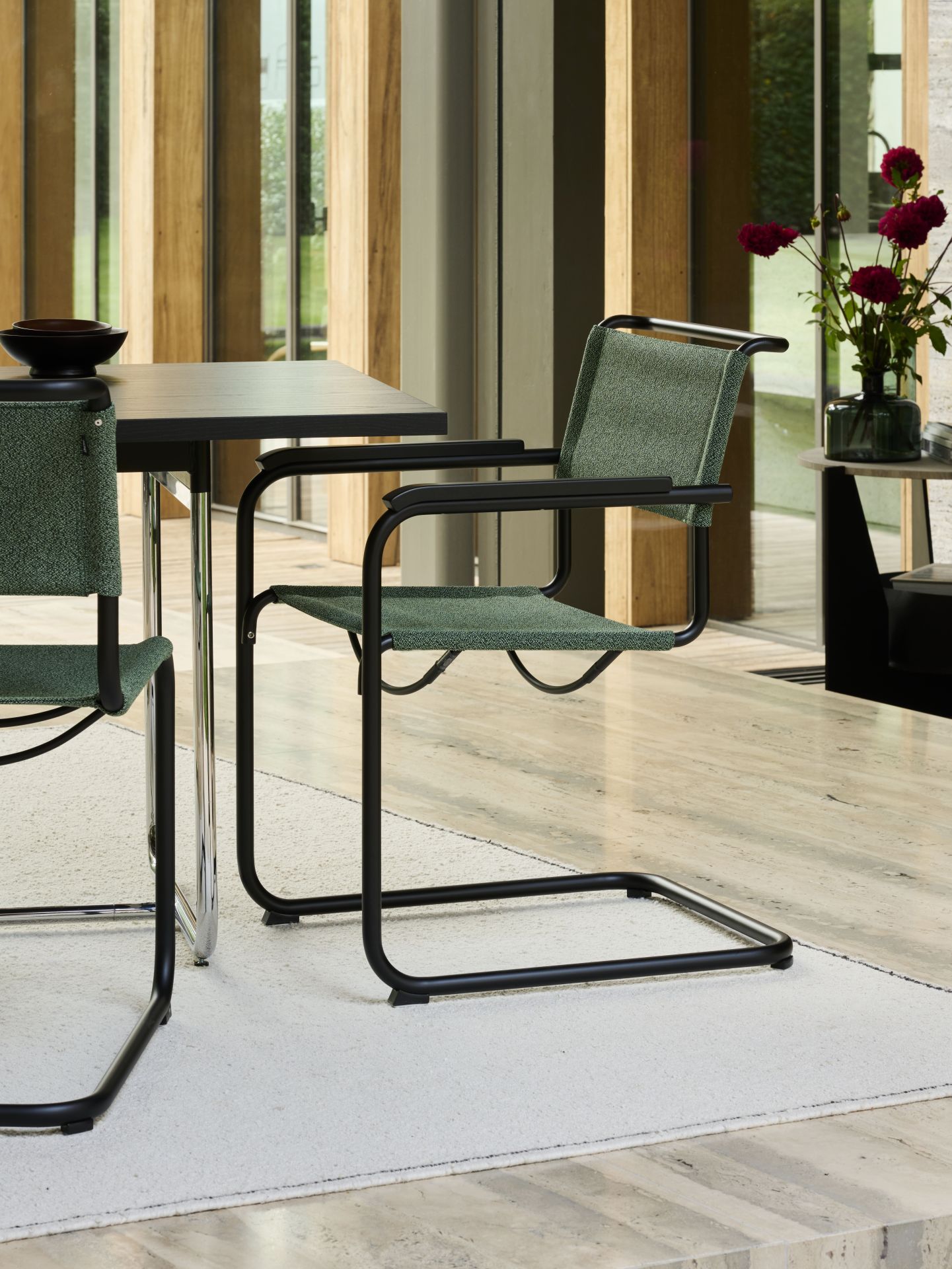 S 34 V Thonet Freischwinger mit grünem Stoffbezug und schwarzem Gestell am Esstisch.