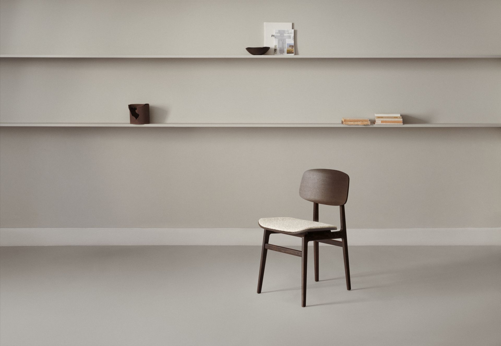 NY11 Stuhl von NORR11, gepolstert, aus dunklem Holz, minimalistisches Design vor Regalwand.