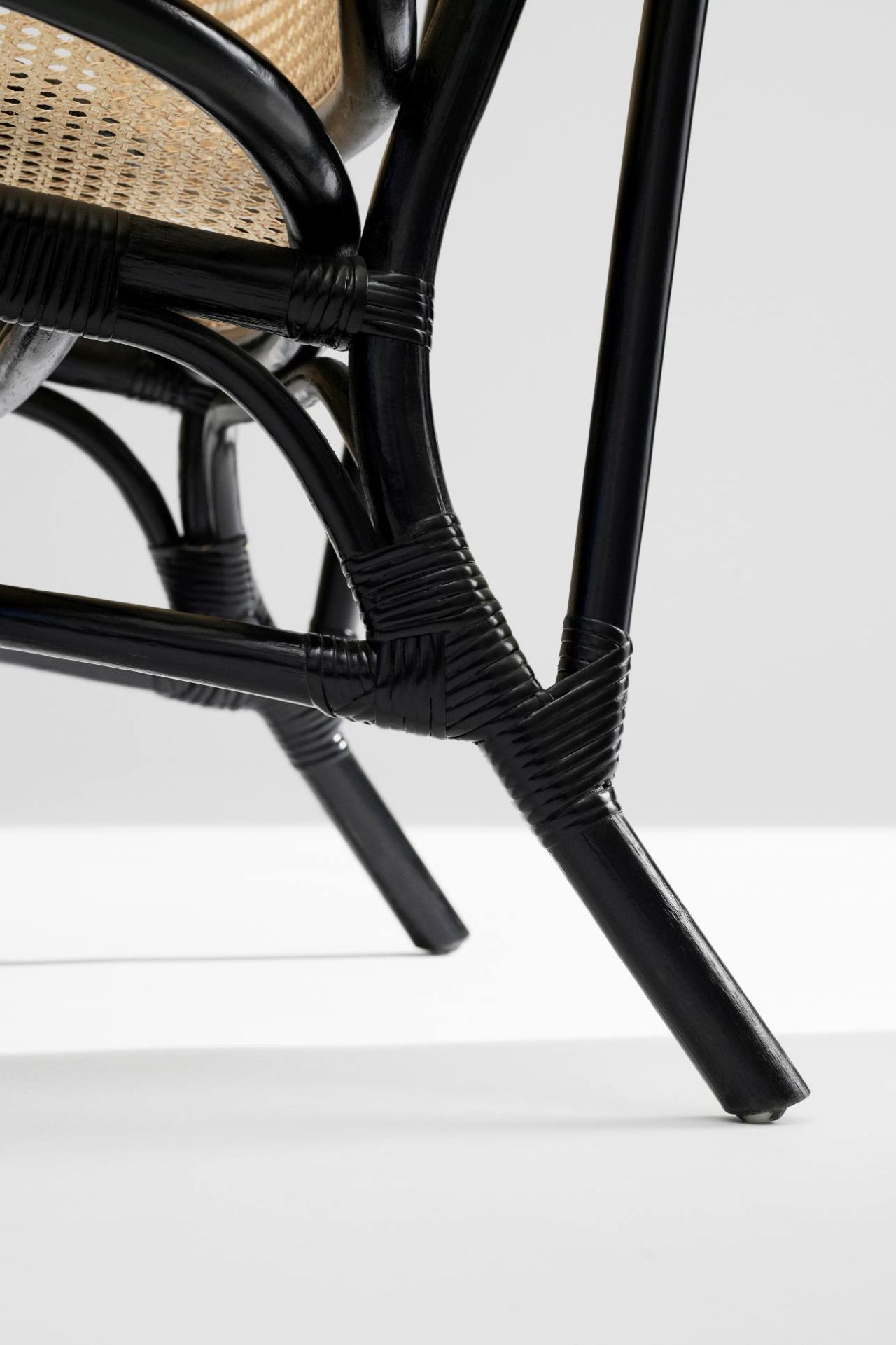 Detailaufnahme des schwarzen Nomad Chair Sessels von NORR11, Fokus auf die Beine und die Rattan-Details.