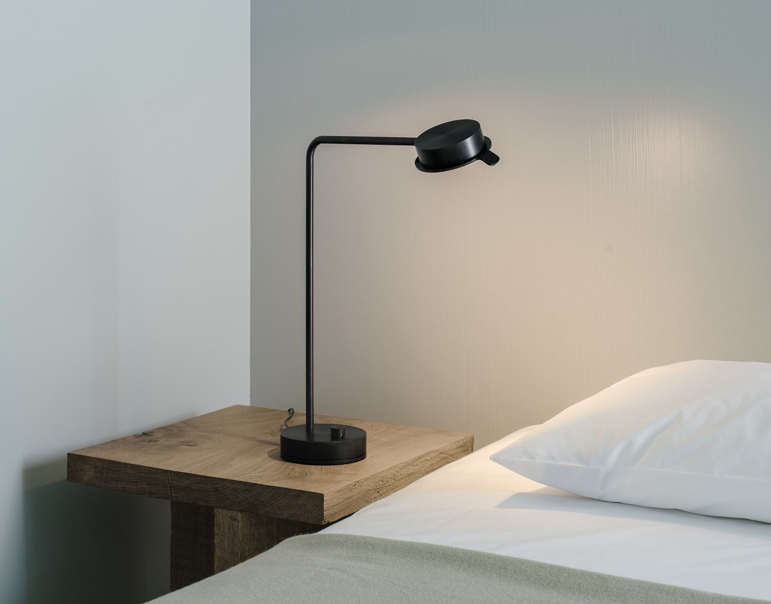 Schwarze w102 B Chipperfield Tischleuchte von wästberg auf Nachttisch neben Bett mit weißem Kissen.