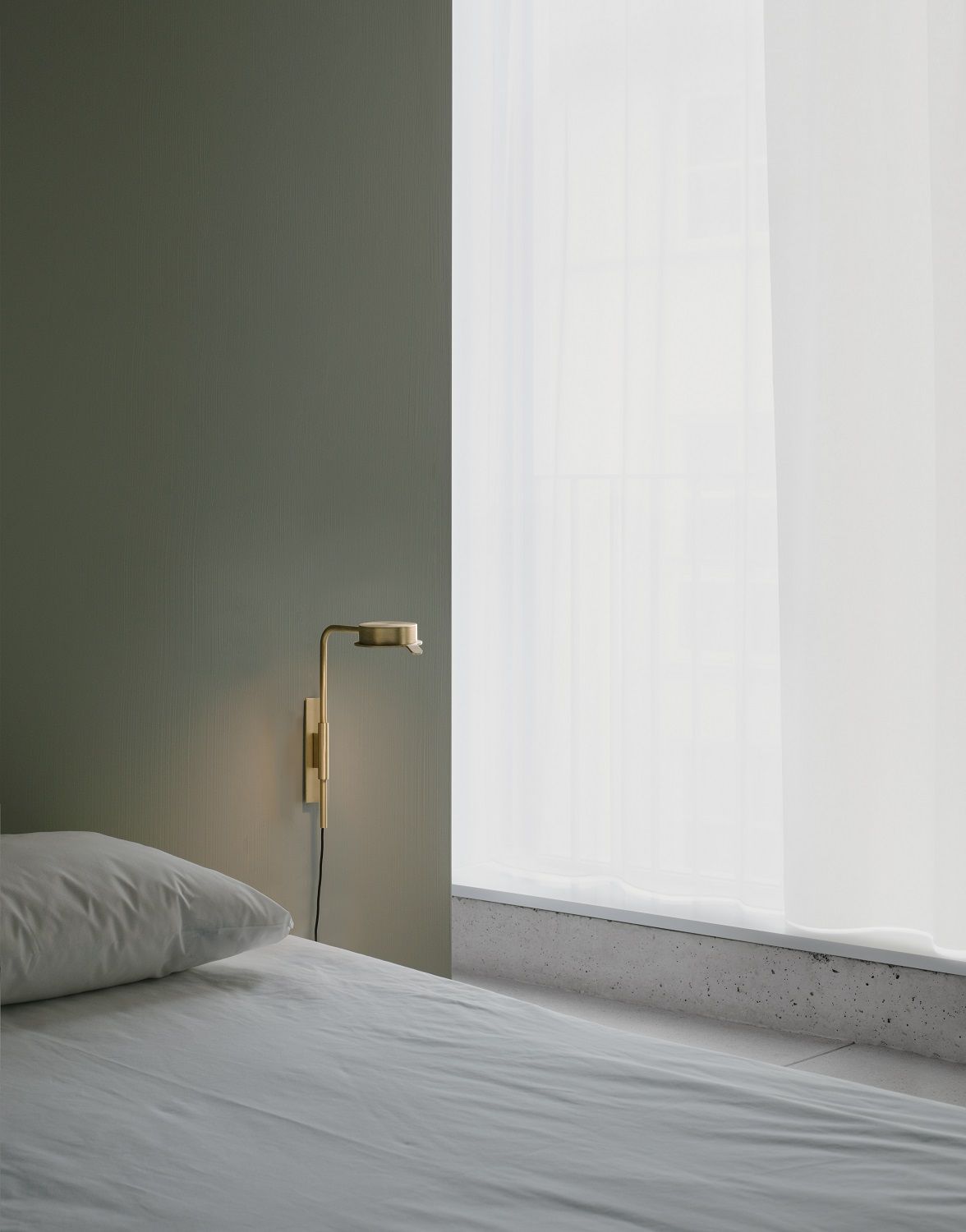 w102 Chipperfield Wandleuchte in Gold neben einem Bett mit weißer Bettwäsche und Vorhang.