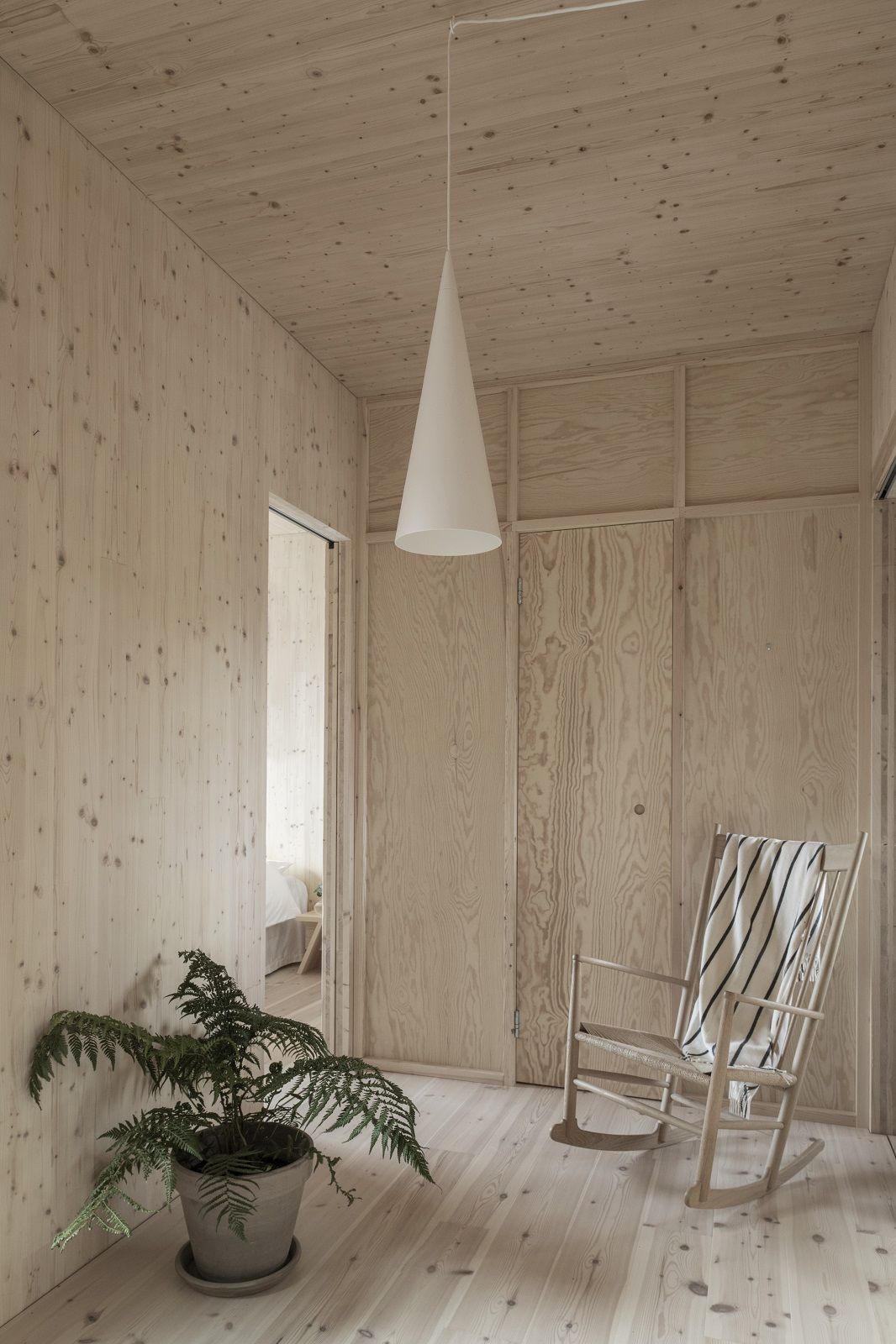 Helle Holzwand mit w221 S1 Medium Pendelleuchte von wästberg, Schaukelstuhl und Zimmerpflanze in modernem Raum.