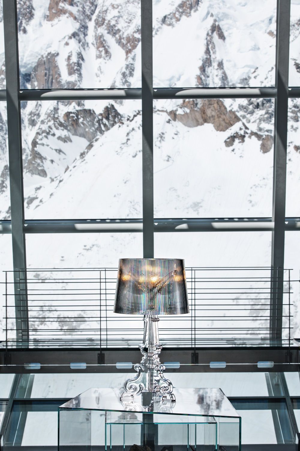 Nahaufnahme der silbernen Kartell Bourgie Tischleuchte mit plissiertem Lampenschirm vor verschneiter Bergkulisse.