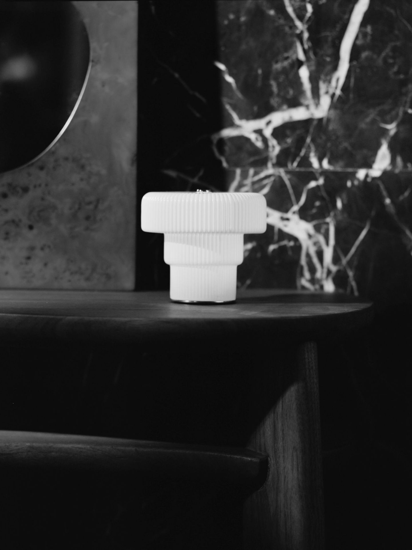 Nahaufnahme der weißen Ripple Tischleuchte von Ferm Living auf einem dunklen Holztisch.